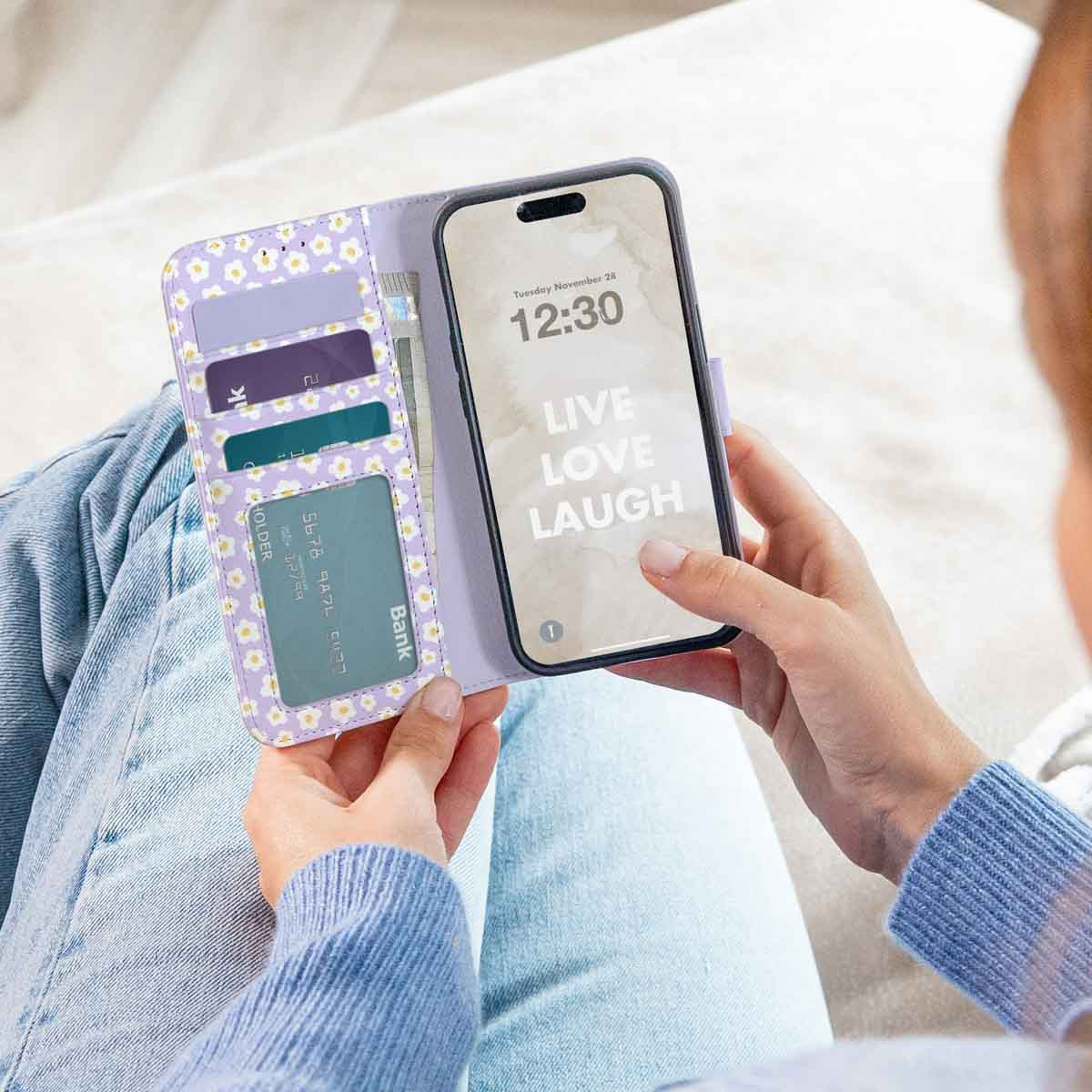 Una persona sostiene una funda de móvil morada con tarjetero y un teléfono con el texto "Live Love Laugh" en la pantalla.