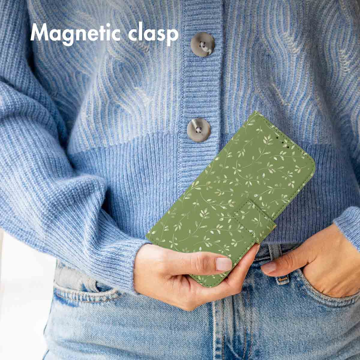 Una persona con suéter azul y jeans sostiene una funda verde para teléfono con patrón de hojas y cierre magnético.