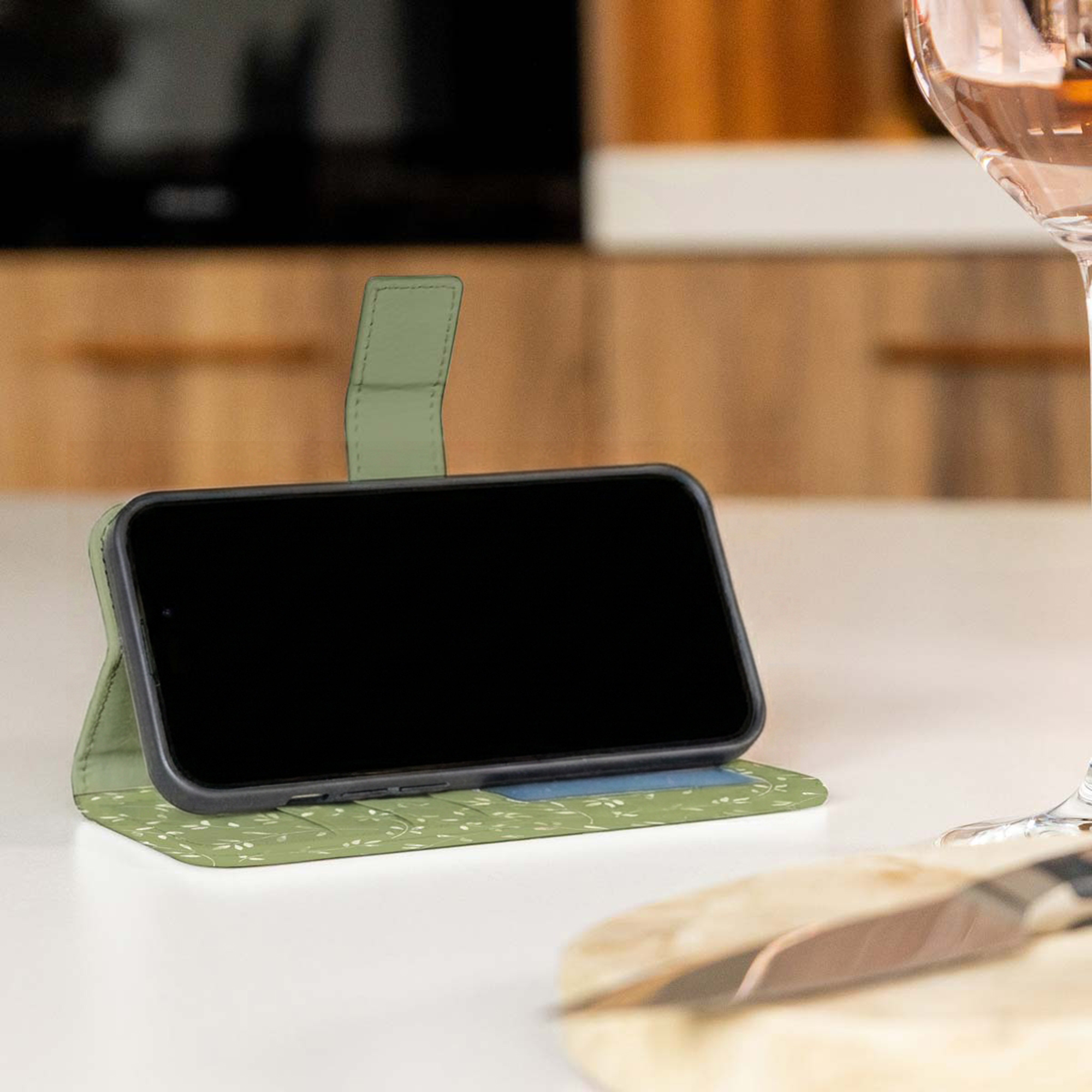 Una funda verde para smartphone con motivo de hojas está sobre una mesa en una cocina.