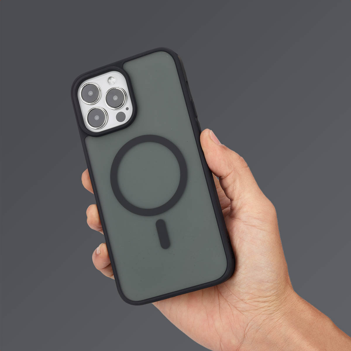 Une main tient un smartphone vert foncé avec coque MagSafe noire sur fond gris.