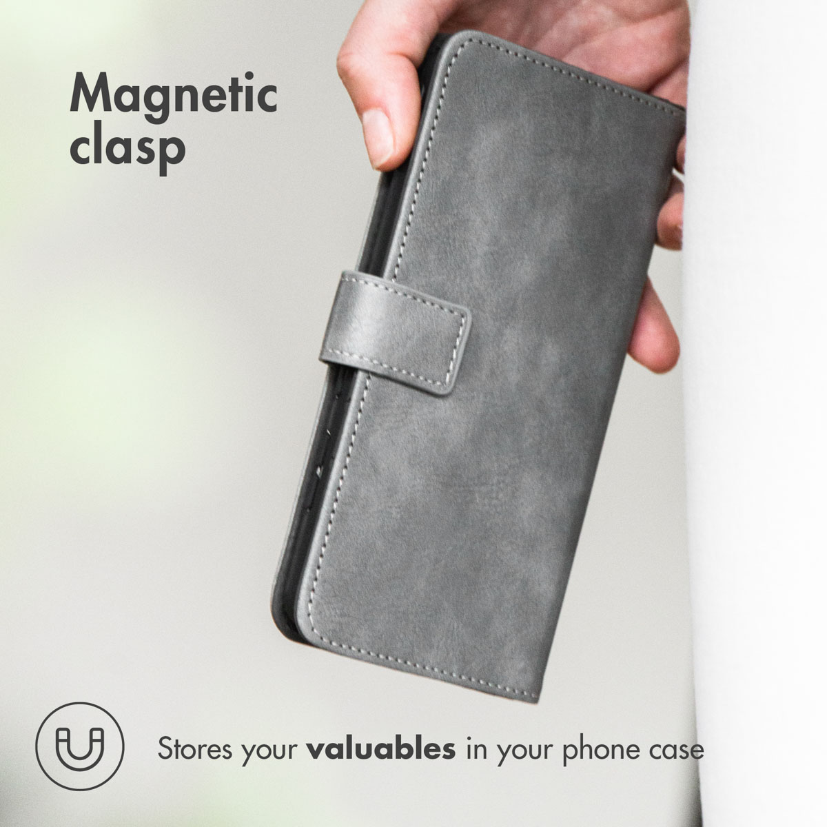 Une main tient un étui de téléphone en cuir gris avec fermoir magnétique, avec du texte sur les fermoirs et objets.