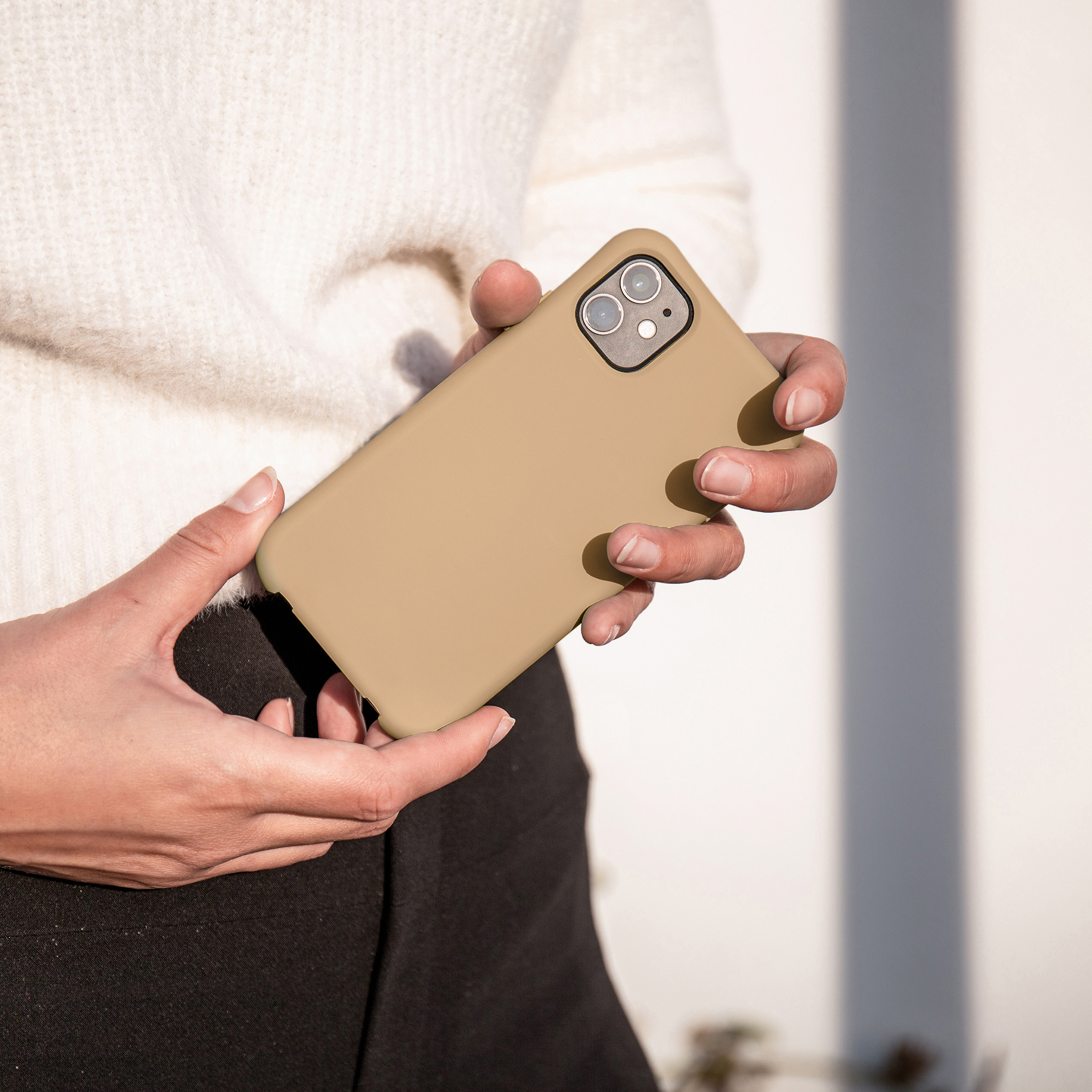 Une personne en pull blanc tient un smartphone beige devant un mur blanc.
