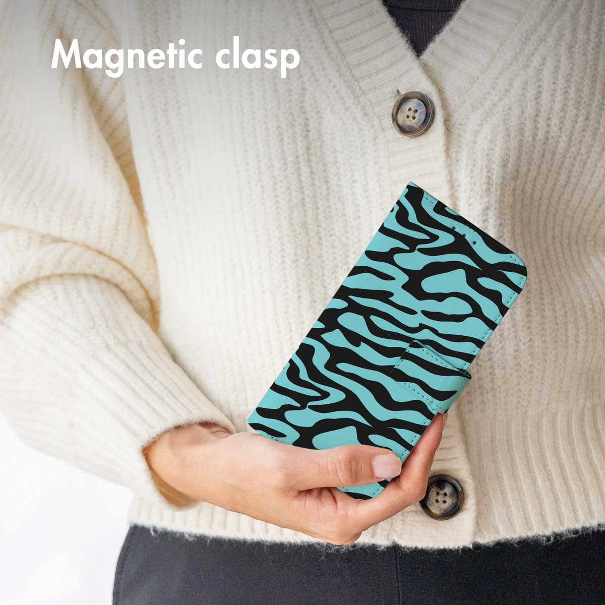 Une personne en cardigan blanc tient un étui de téléphone turquoise à zébrures noires.