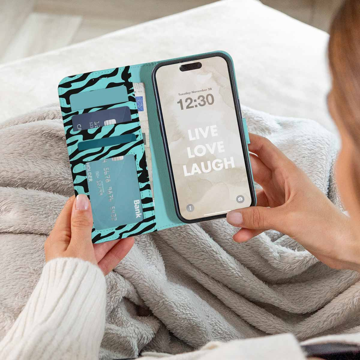 Une femme tient un étui de téléphone vert menthe à motif zébré avec fentes pour cartes, assise sur une couverture duveteuse.