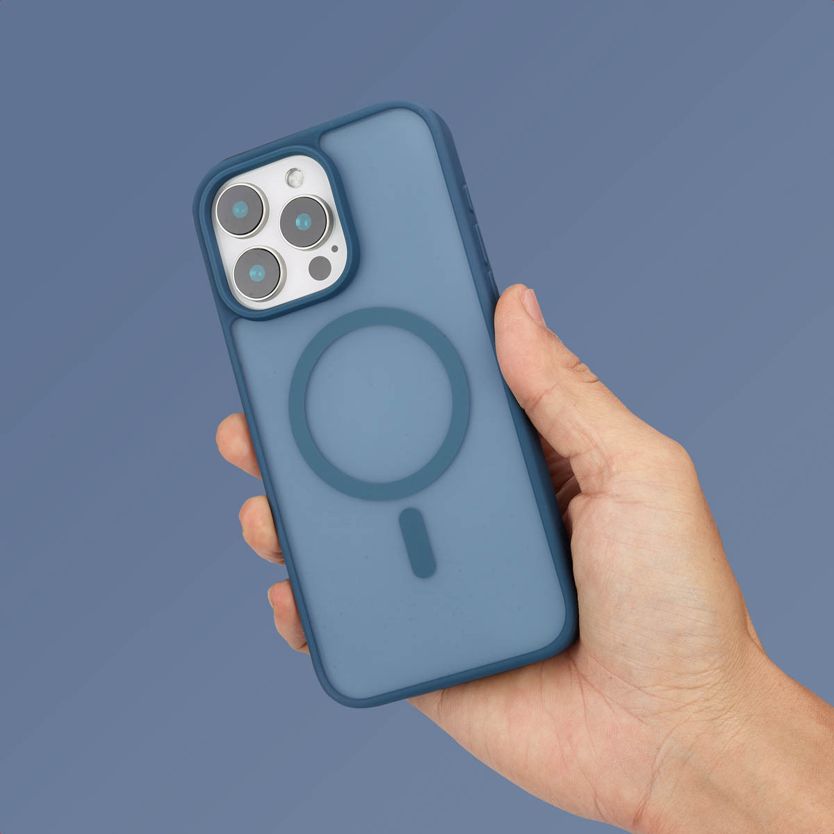 Une main tient un smartphone bleu avec une coque MagSafe et triple appareil photo sur fond gris.