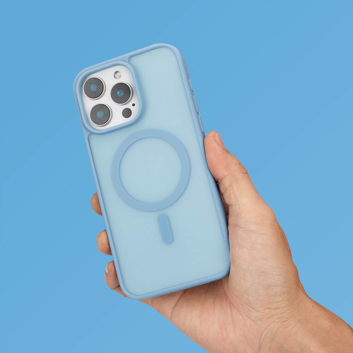 Een hand houdt een lichtblauwe smartphone in een siliconenhoes met MagSafe-ring tegen een blauwe achtergrond.