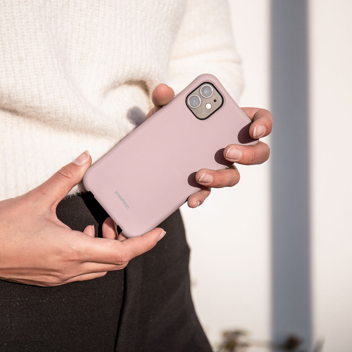 Personne en pull blanc tenant un smartphone rose dans ses mains.