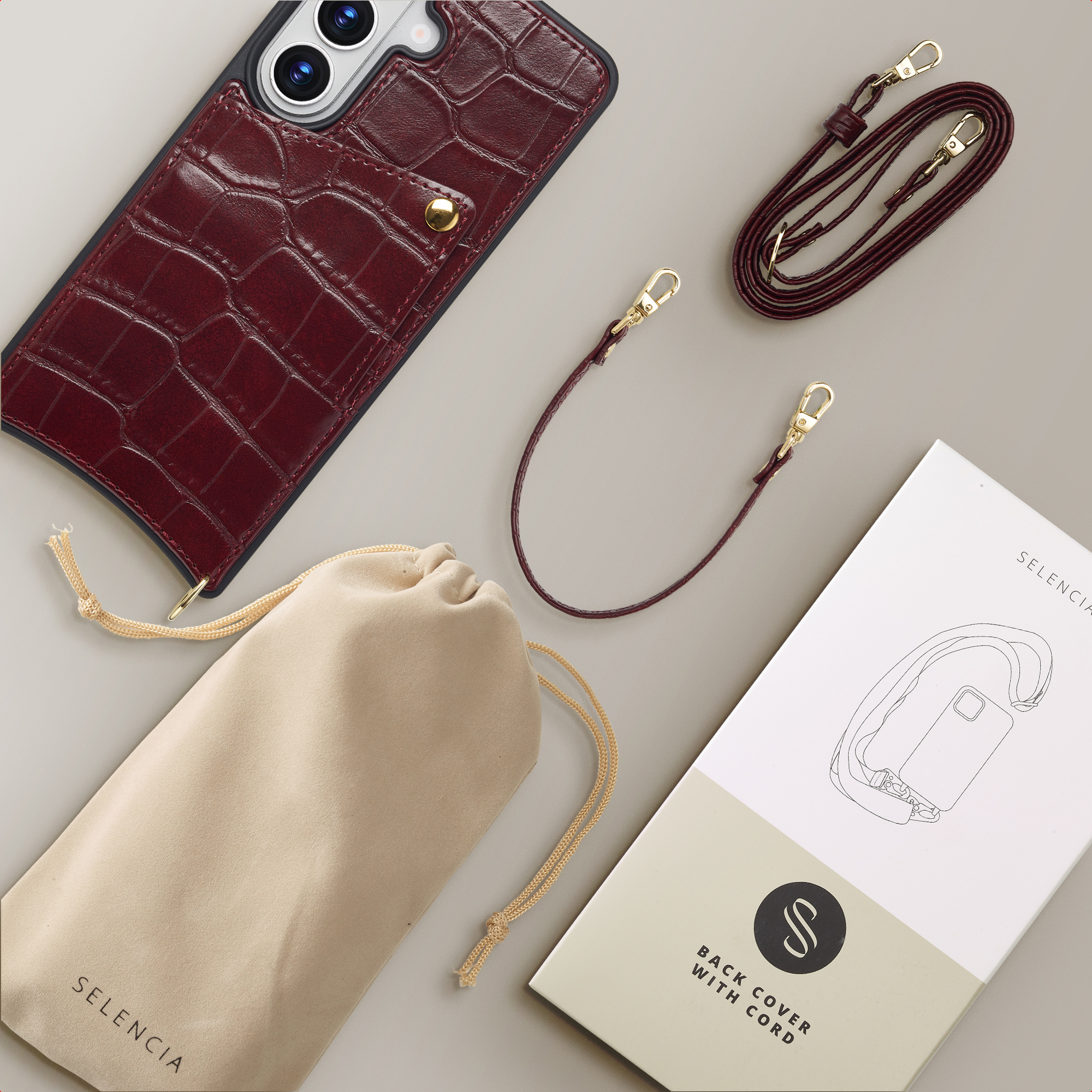 Funda de teléfono de cocodrilo burdeos con dos correas, una bolsa y envase sobre fondo claro.