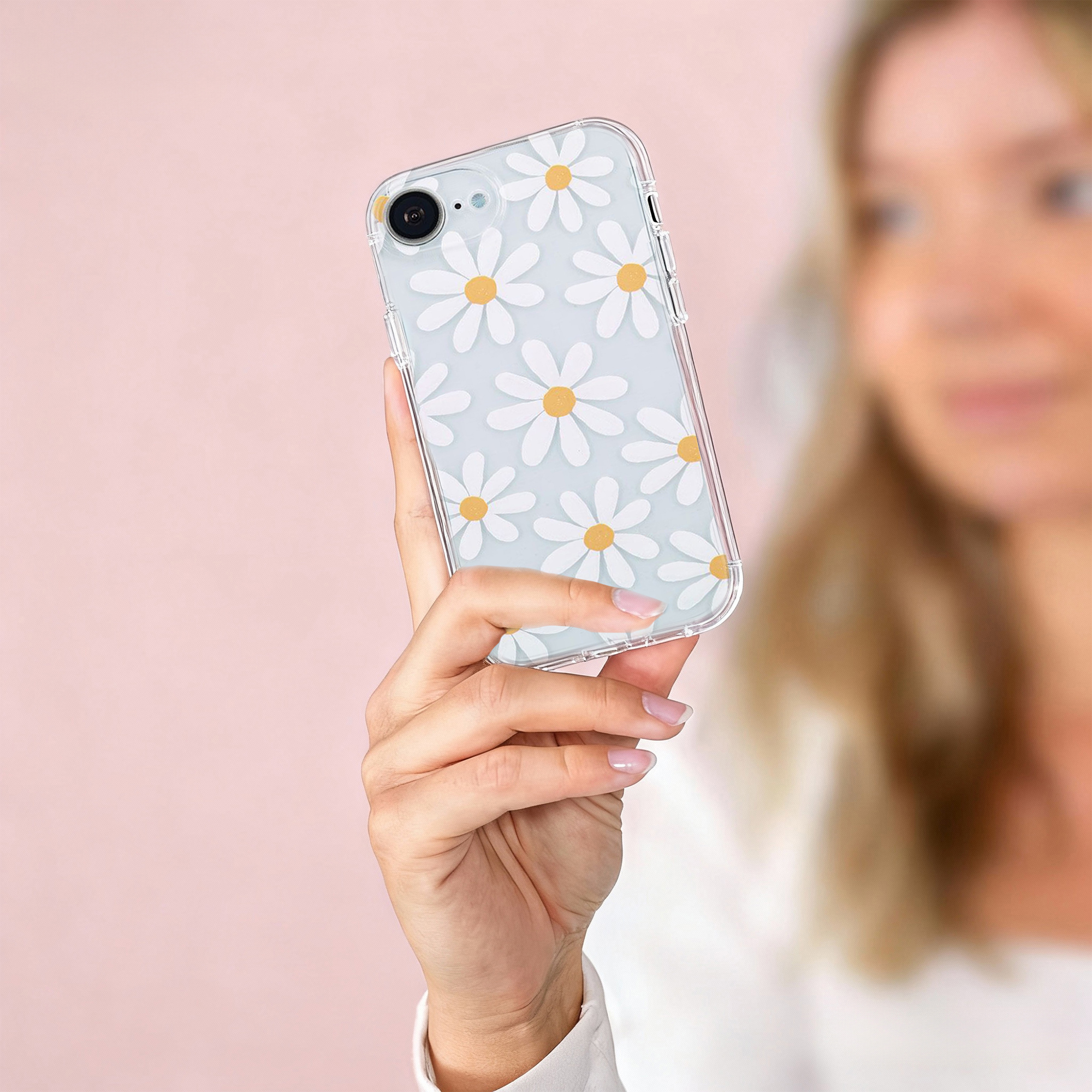 Une femme tient un téléphone avec une coque transparente à motif de marguerites sur fond rose.