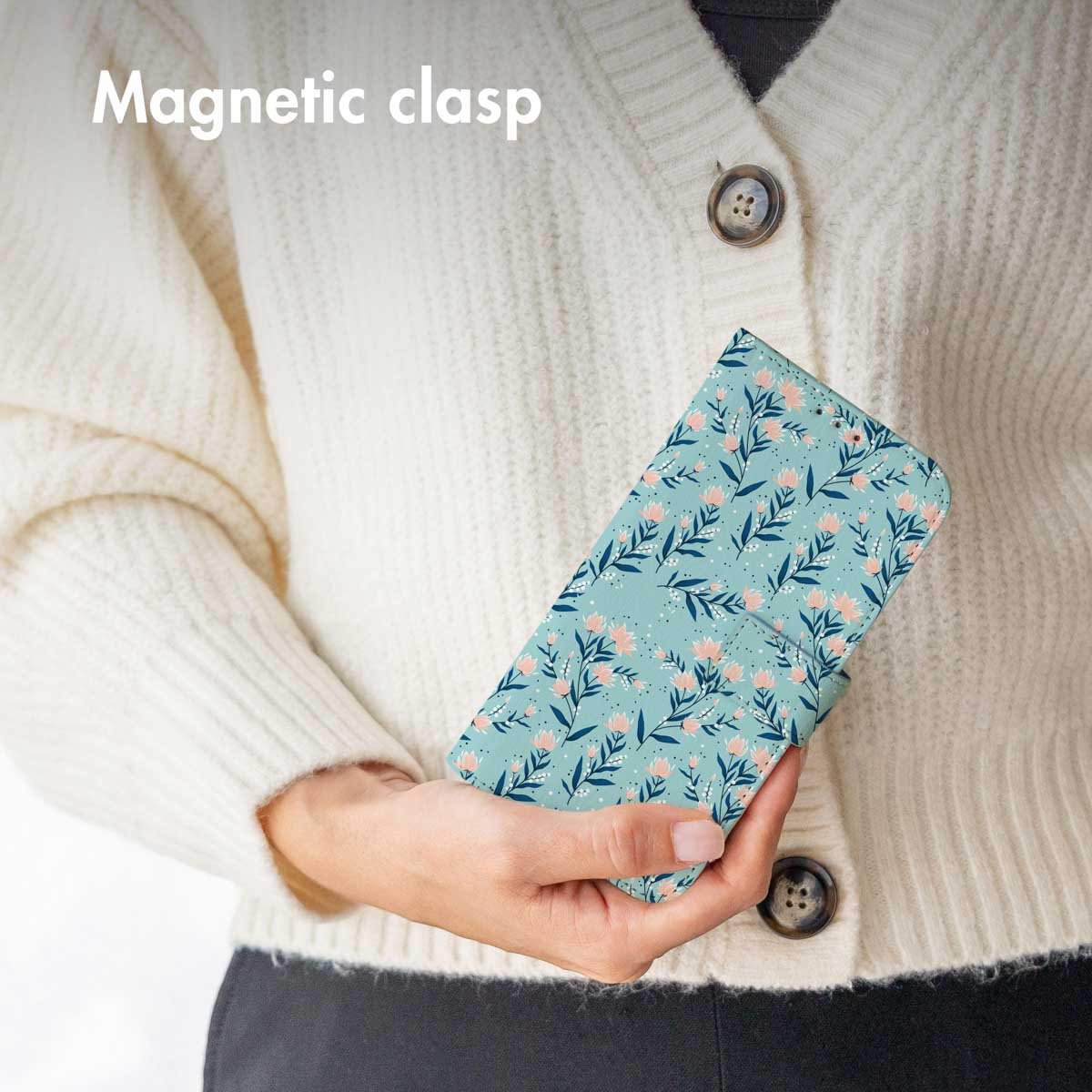 Persona con suéter blanco sostiene funda de móvil azul con flores rosas y texto.