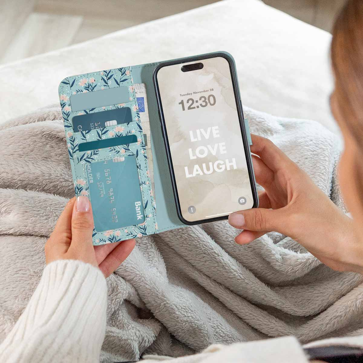 Una mujer sostiene una funda de móvil tipo cartera con estampado floral, tarjetero y un smartphone.