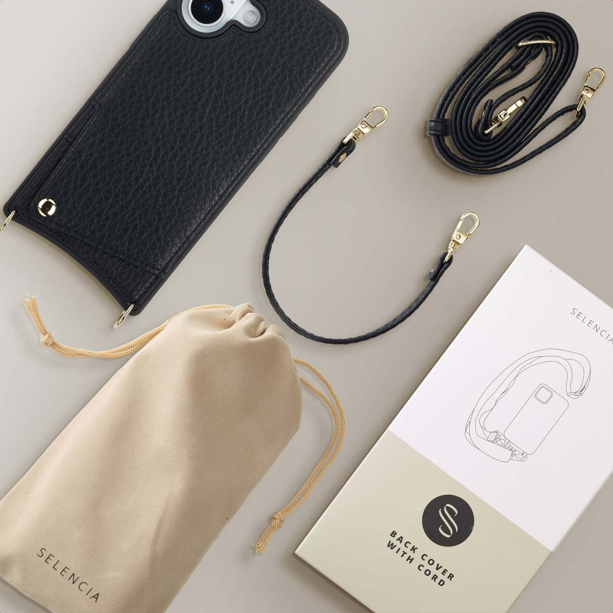 Funda de móvil negra, dos correas negras, bolsa beige y caja de producto Selencia sobre un fondo beige neutro.