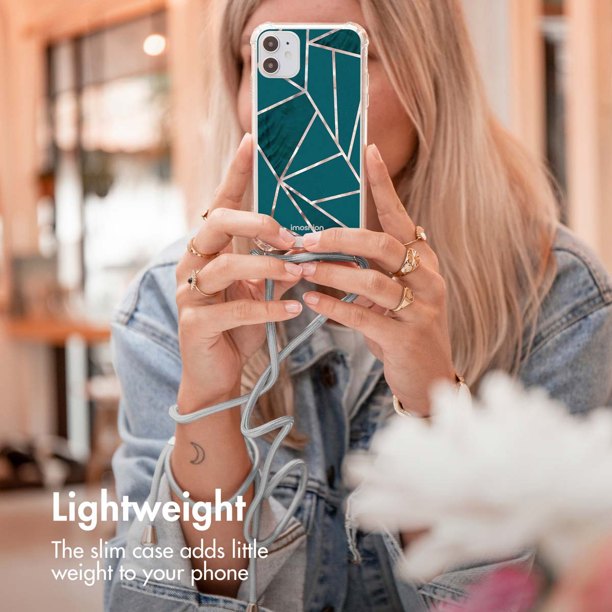 Une femme blonde tient un smartphone avec une coque verte et dorée et une lanière.