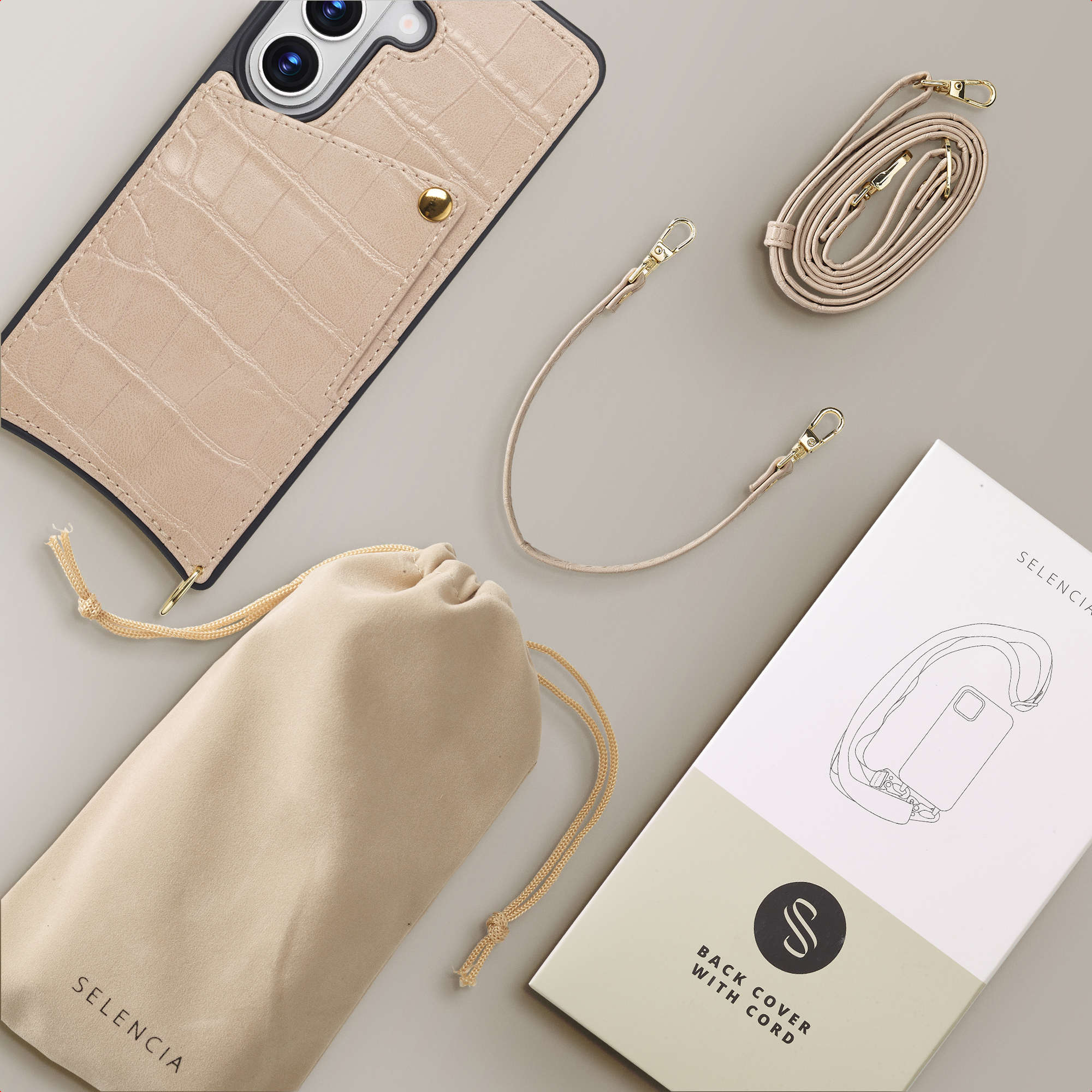 Funda de móvil beige con tarjetero, dos correas, bolsa con cordón y caja de producto en superficie neutra.