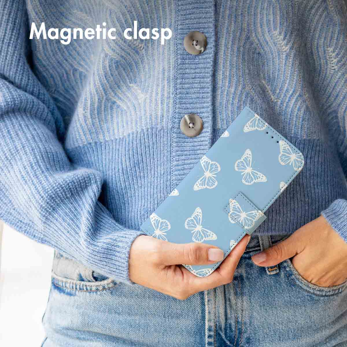 Une personne en gilet bleu et jean tient une coque de téléphone bleu clair avec des papillons blancs.