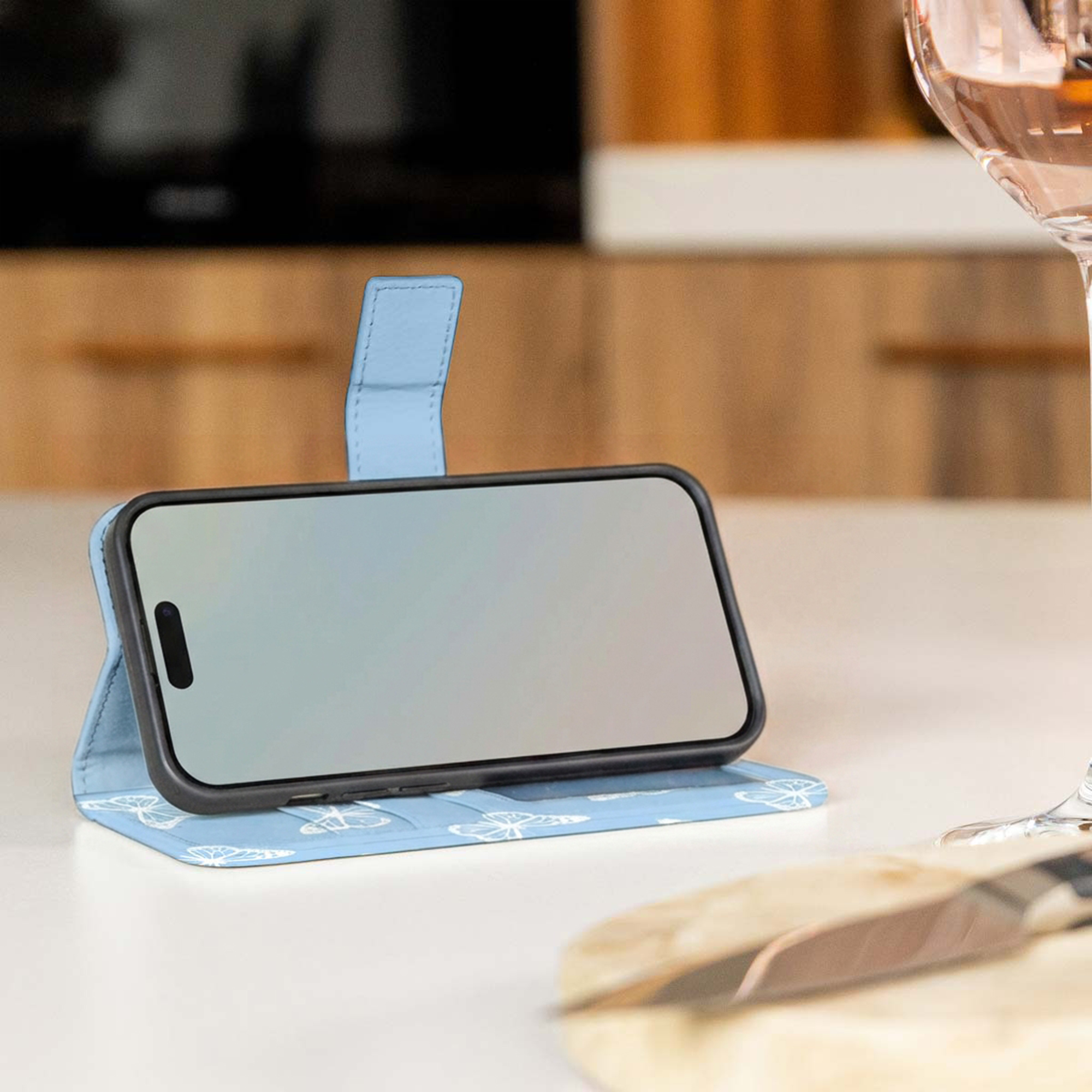 Un étui de téléphone bleu avec un motif de papillons sur une table, avec un verre de vin.