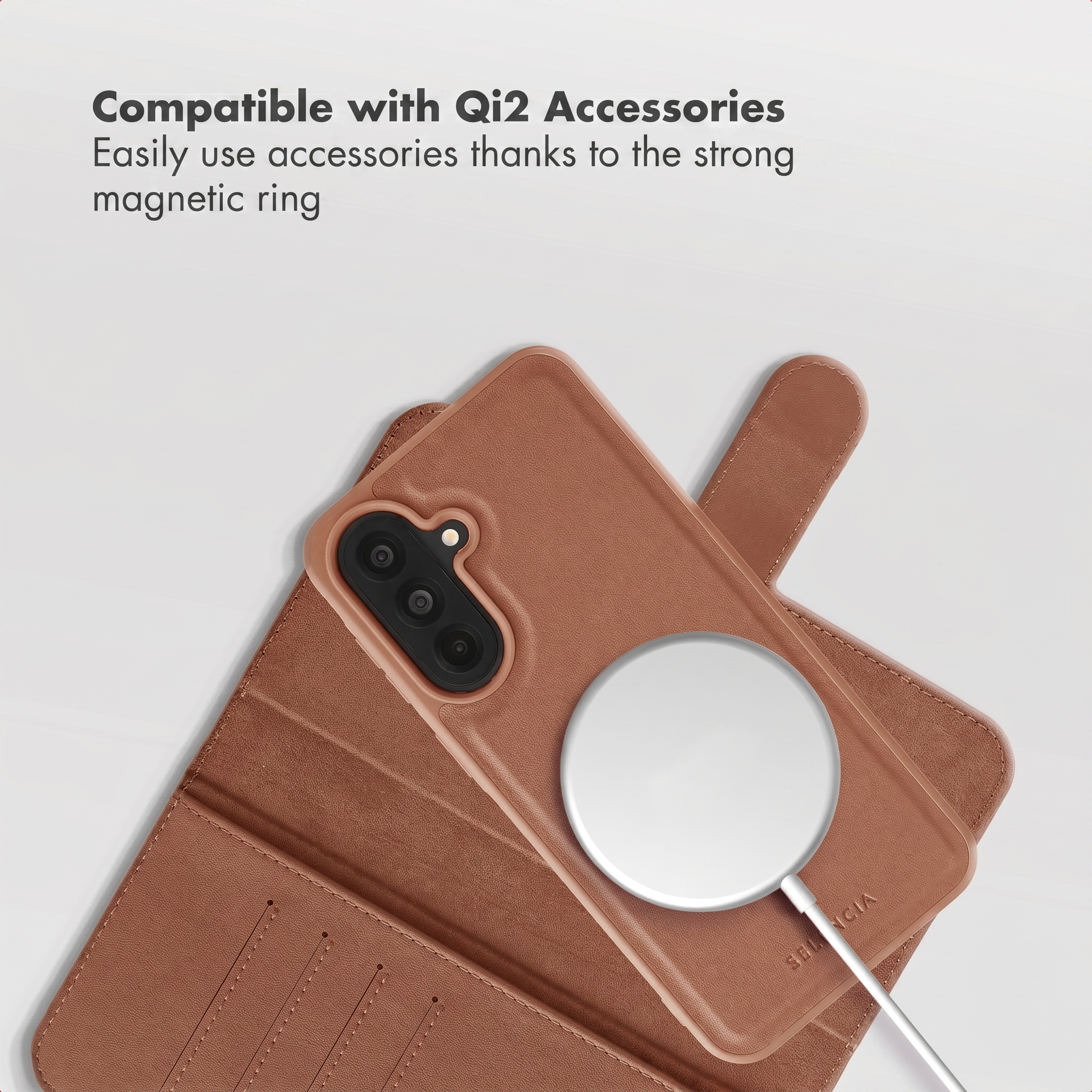 A brown leather smartphone case with a round white magnetic charger on the back against a gray background.