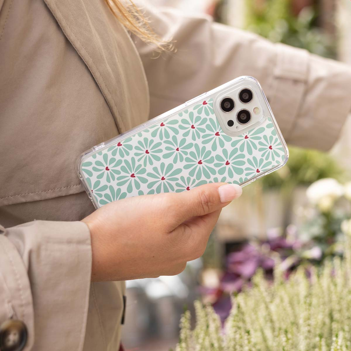 Una persona con abrigo sostiene un smartphone con patrón floral y de corazones verde menta.