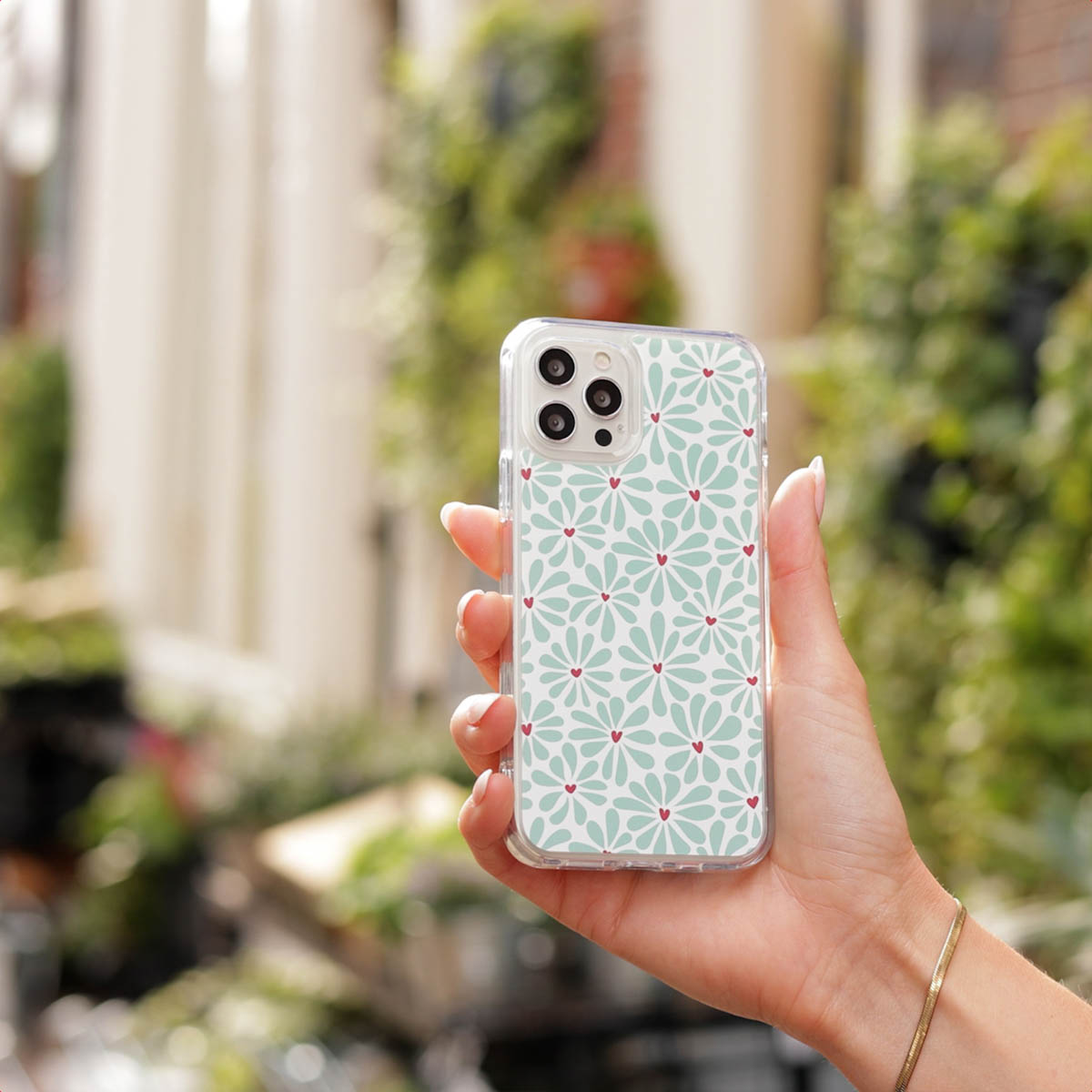 Una mano sostiene un teléfono inteligente con funda protectora de patrón floral y pequeños corazones rojos.