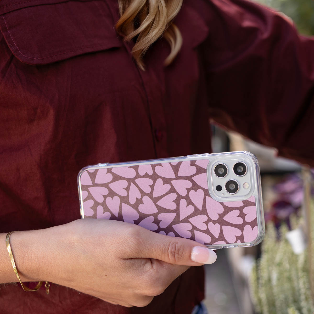 Una mujer con camisa burdeos sostiene un teléfono con una funda de corazones rosas.