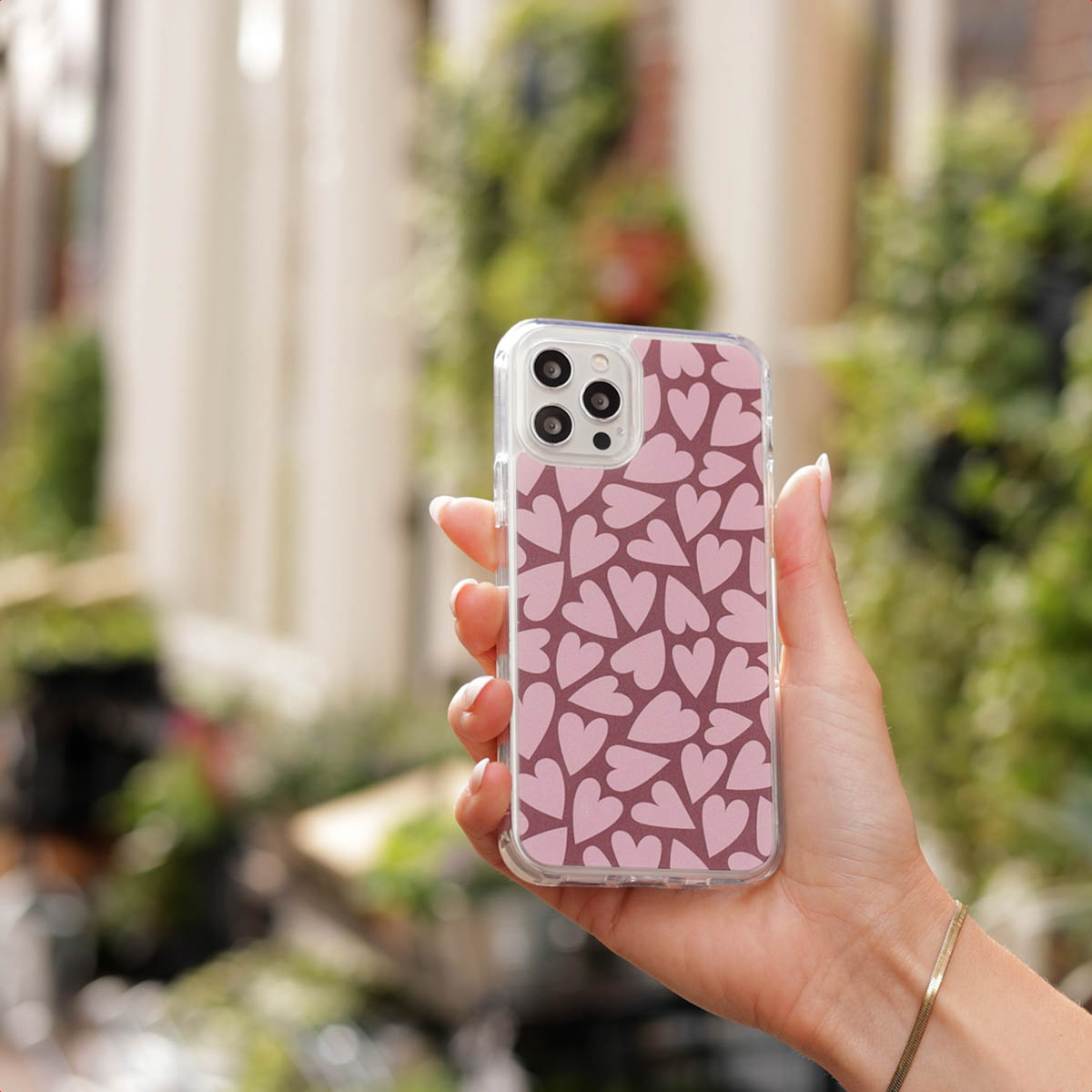Una mano sostiene un teléfono con funda rosa de corazones ante un fondo borroso.