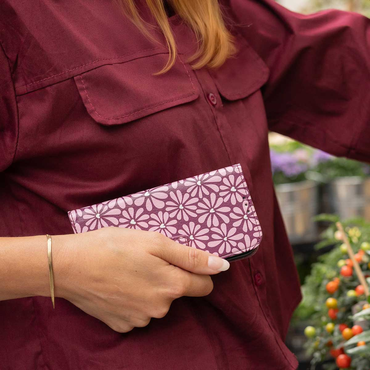 Eine Person in einem dunkelroten Hemd hält ein rosa Portemonnaie mit weißem Gänseblümchenmuster.