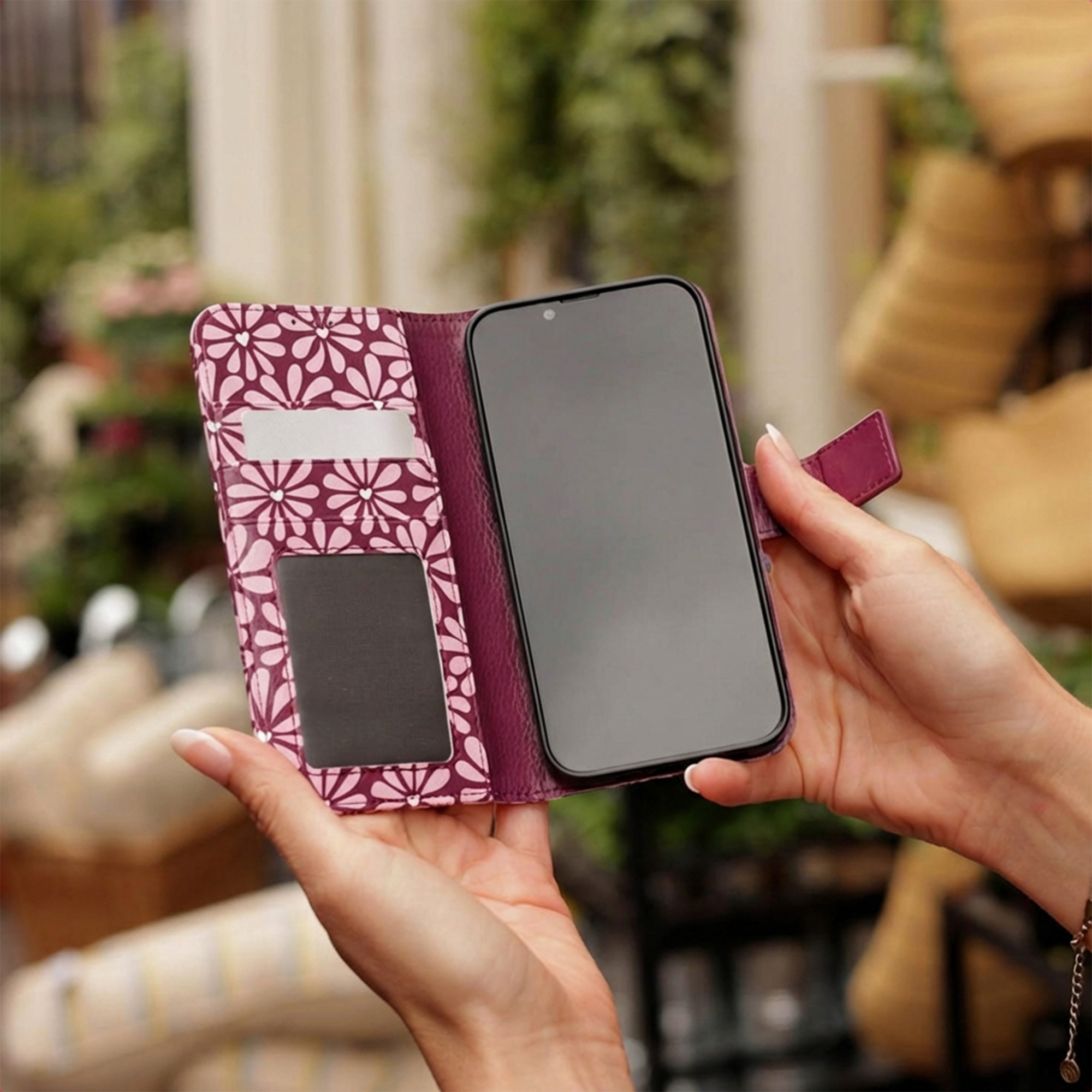 Person hält eine offene lila Handytasche mit weißem Blumenmuster, Einsteckfächern und einem Smartphone in Händen.