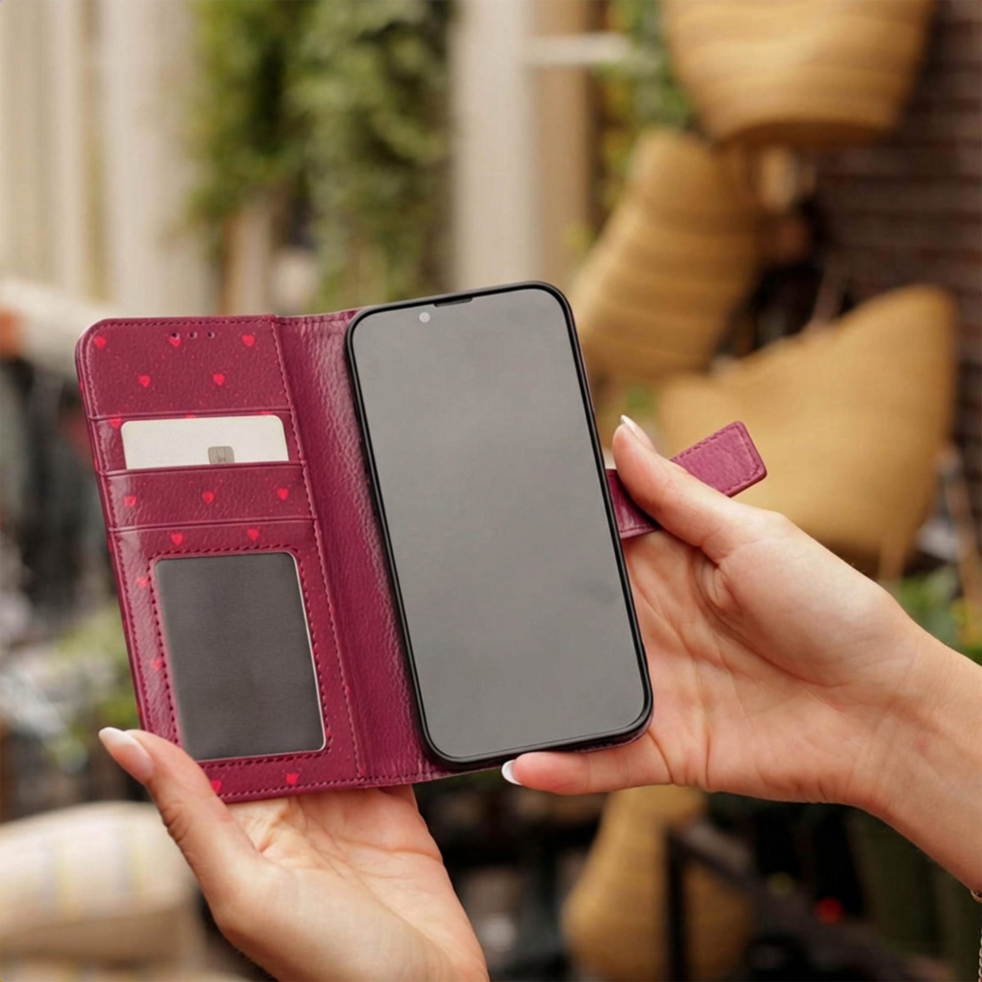 Eine Hand hält eine burgunderrote Leder-Handyhülle mit Kartenfächern und einem Smartphone.