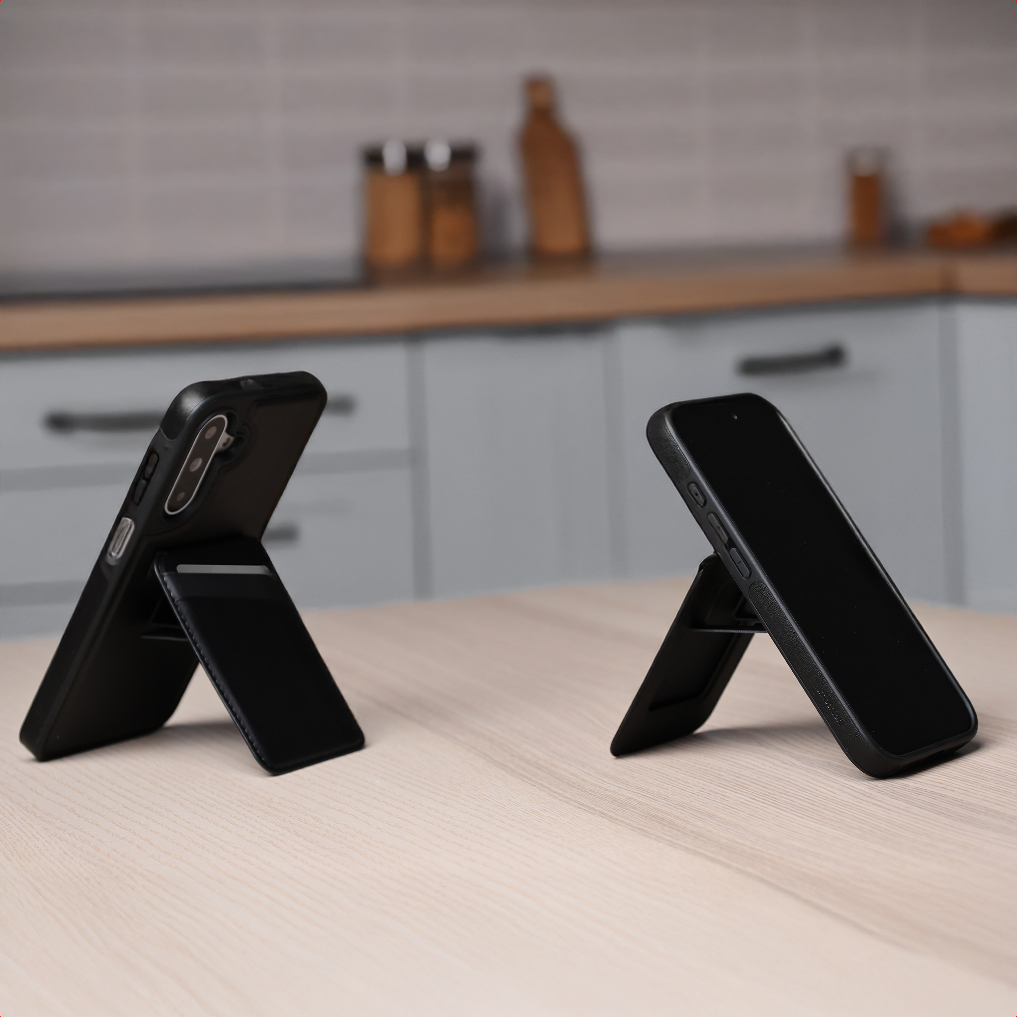 Due smartphone neri su supporti, uno con fotocamera posteriore e l'altro con schermo, su un tavolo di legno.