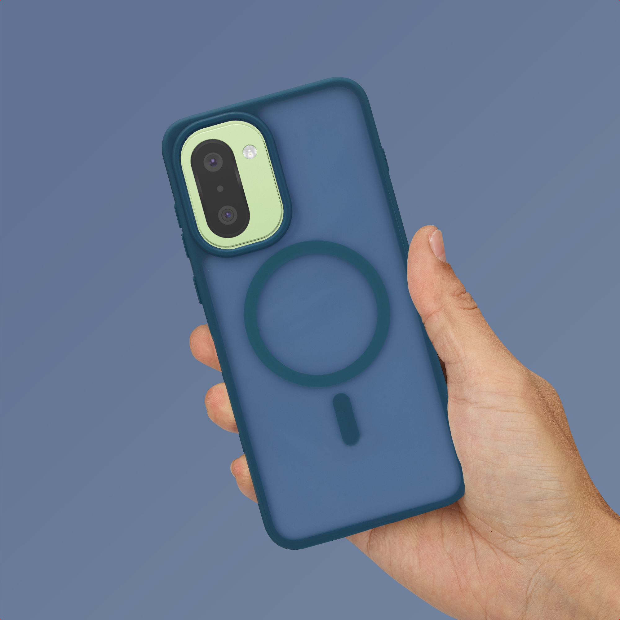 Mano sosteniendo un smartphone azul con módulo de cámara verde claro y anillo MagSafe sobre fondo gris.