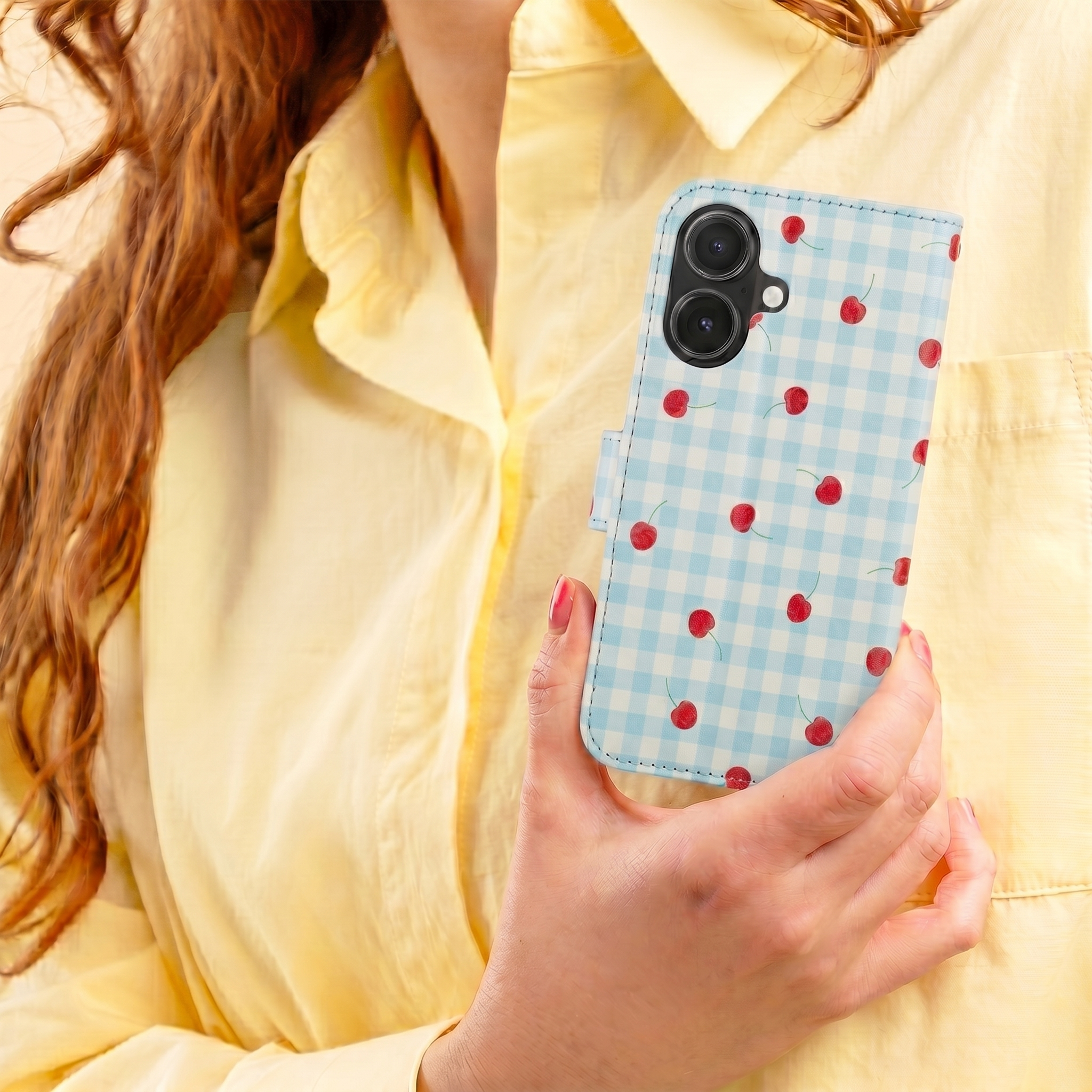 Eine Frau in gelbem Hemd hält ein blau-weiß kariertes Handycover mit roten Kirschen.