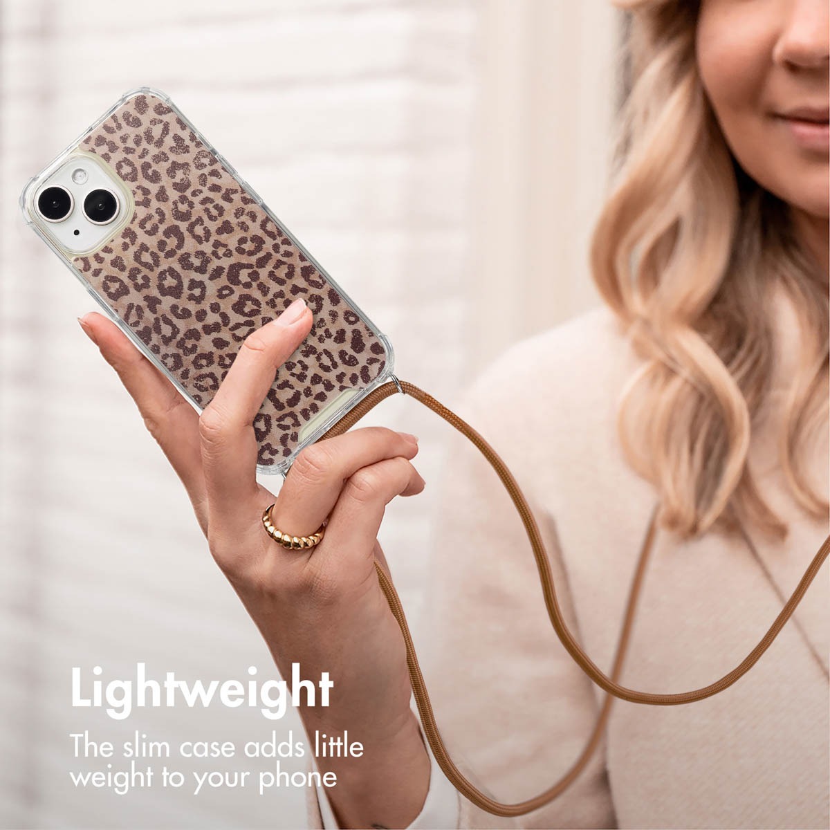 Una donna tiene in mano uno smartphone con cover leopardata e laccetto marrone.