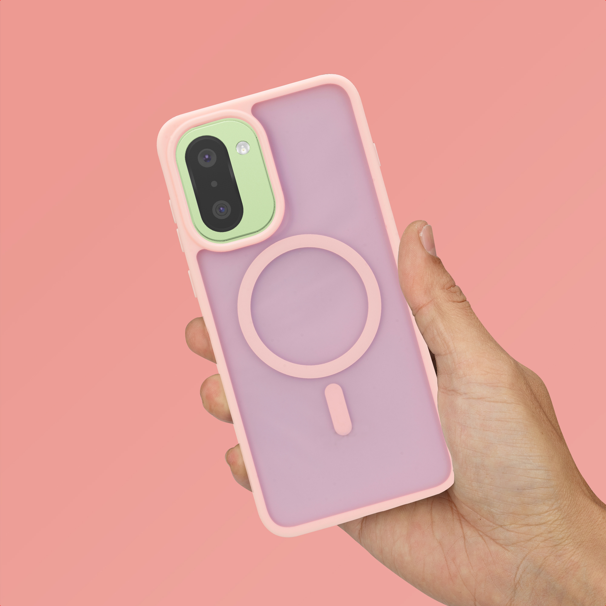 Una mano sostiene una funda de teléfono rosa con un módulo de cámara verde sobre fondo rosa.
