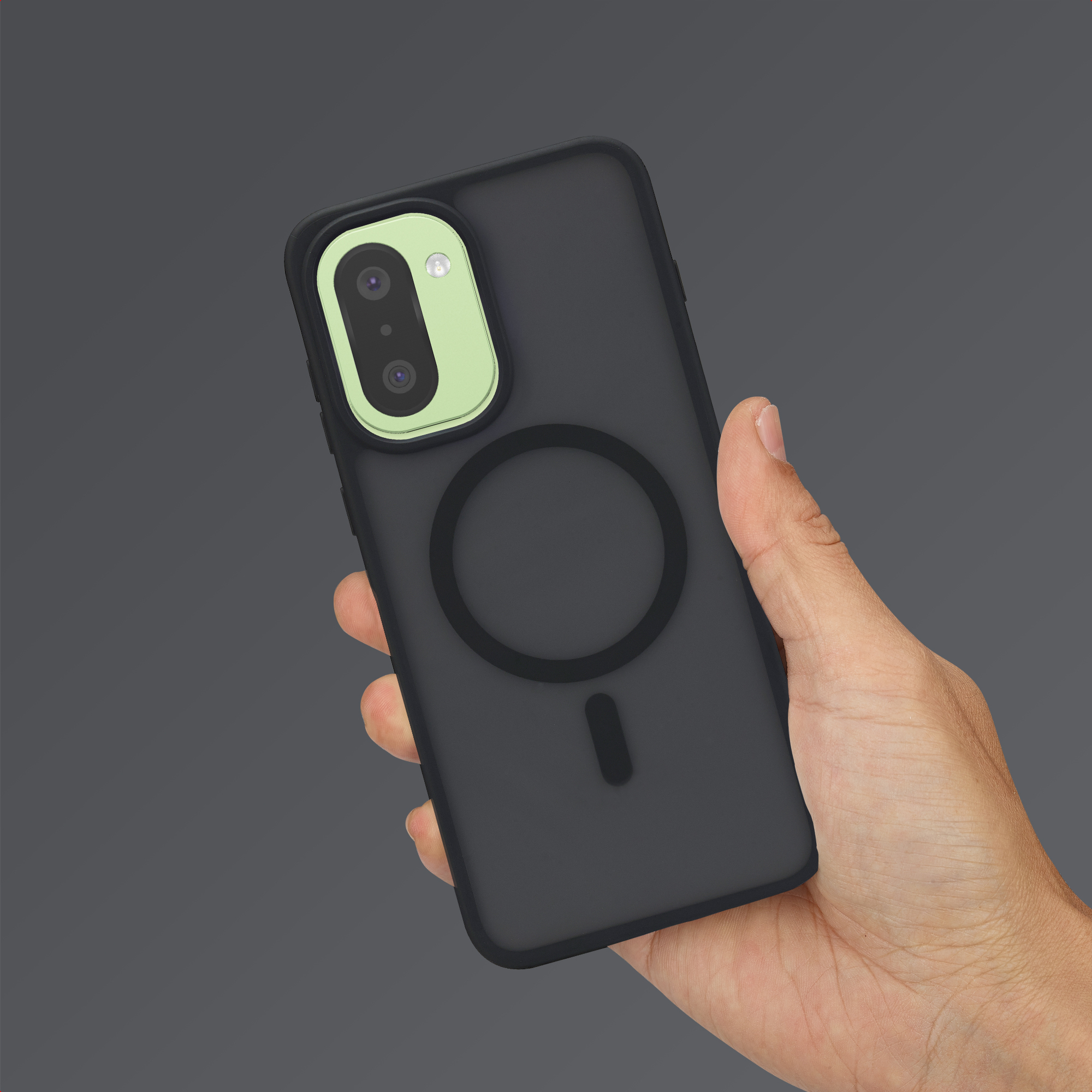 Una mano sostiene un teléfono negro con un marco de cámara verde claro y un anillo MagSafe.
