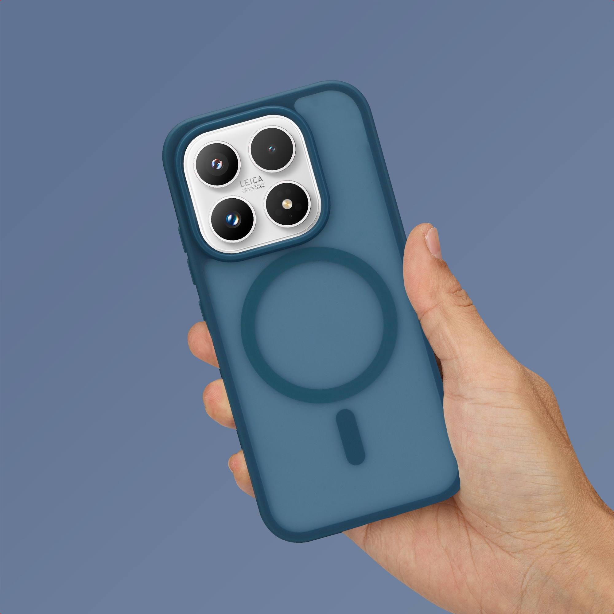 Una mano sostiene un smartphone azul con cuatro lentes de cámara y un logo MagSafe circular sobre fondo gris.