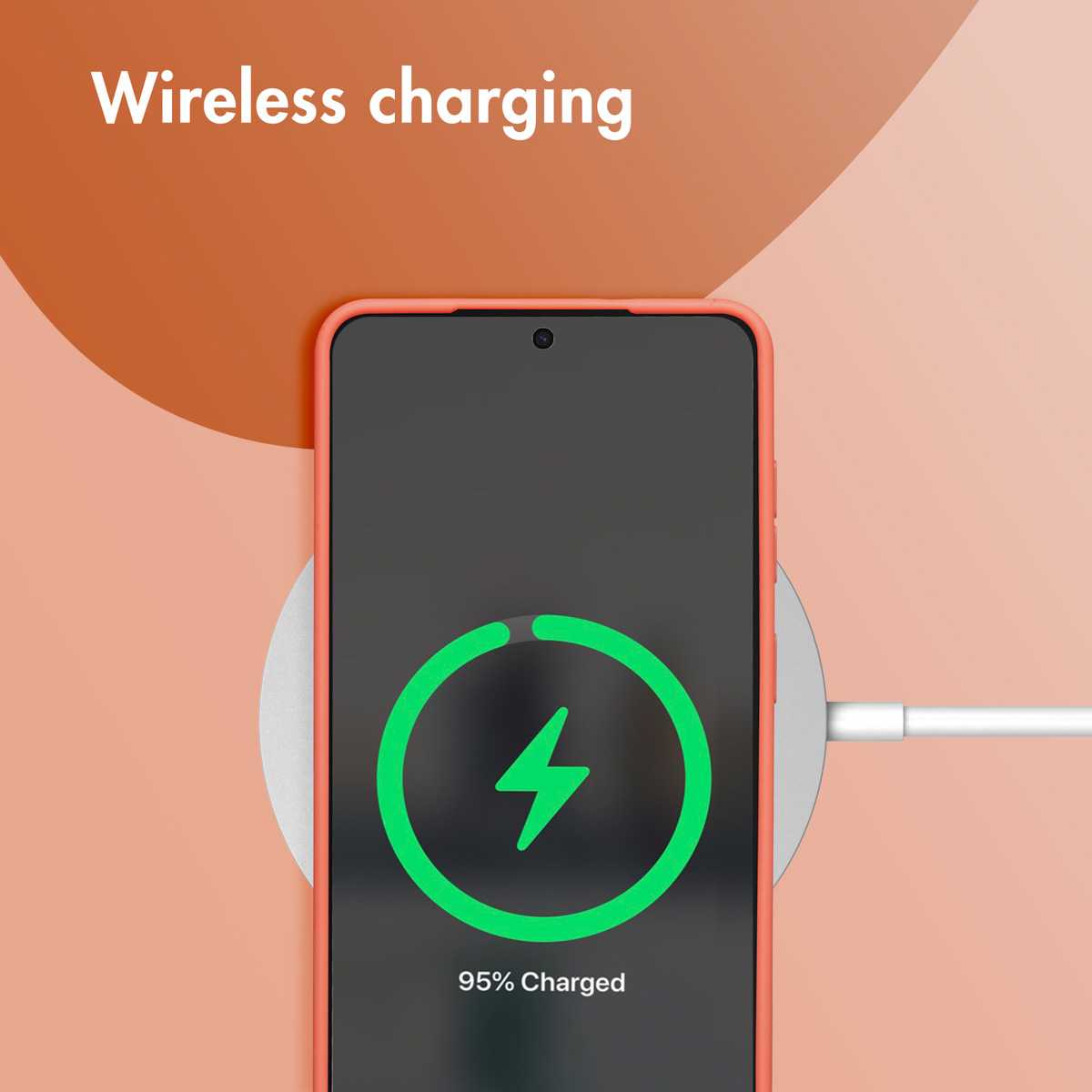 Un teléfono naranja cargándose de forma inalámbrica en una base redonda sobre un fondo color melocotón.