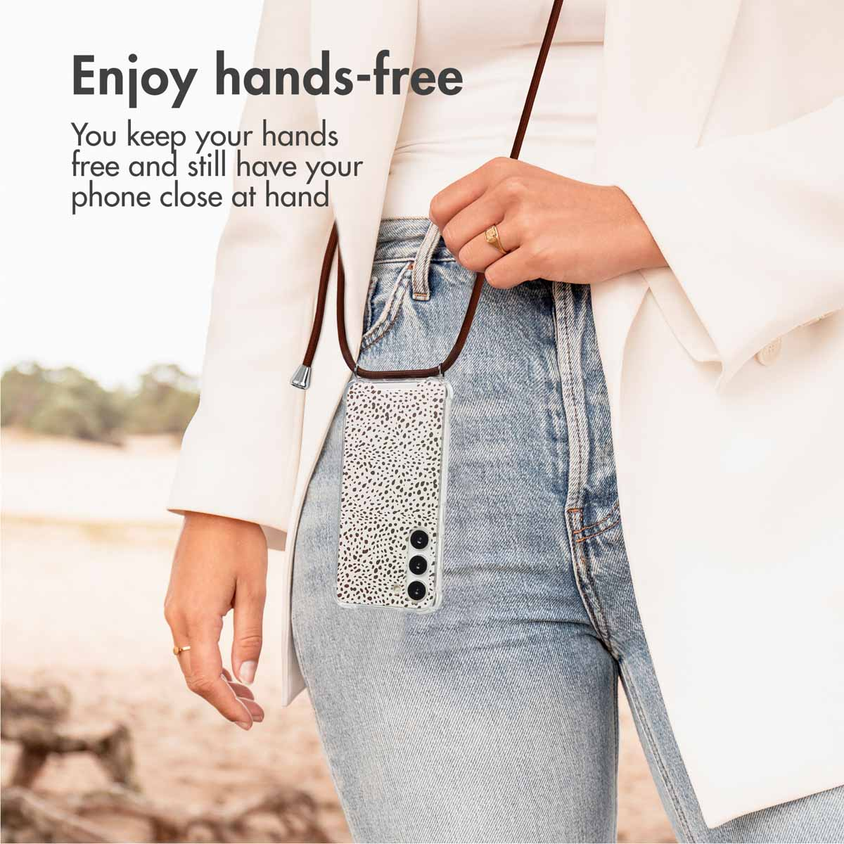 Une femme en veste blanche et jean porte un smartphone avec lanière. Texte: Enjoy hands-free.