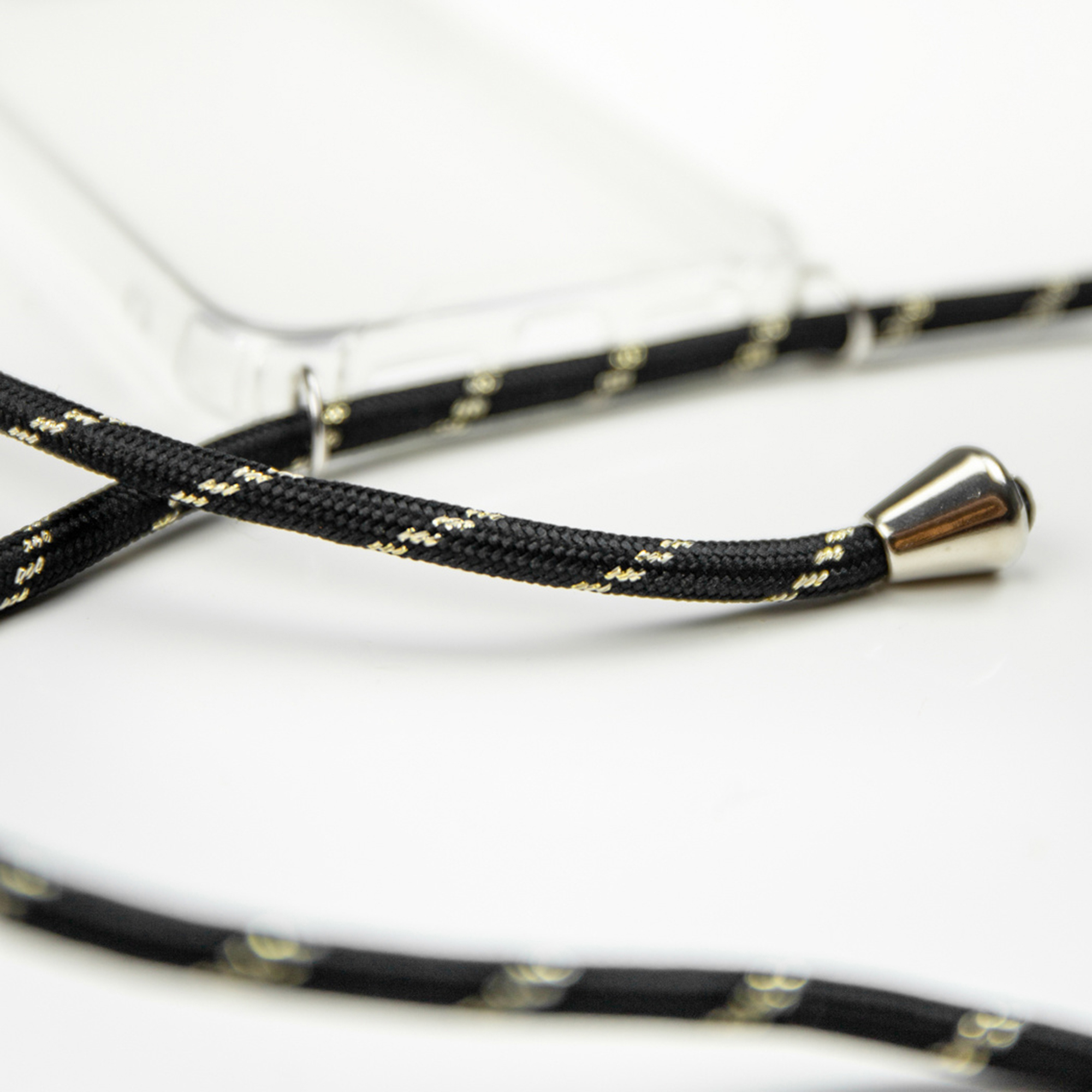 Una correa de cordón negro y dorado con extremos plateados ante una funda transparente sobre fondo blanco.