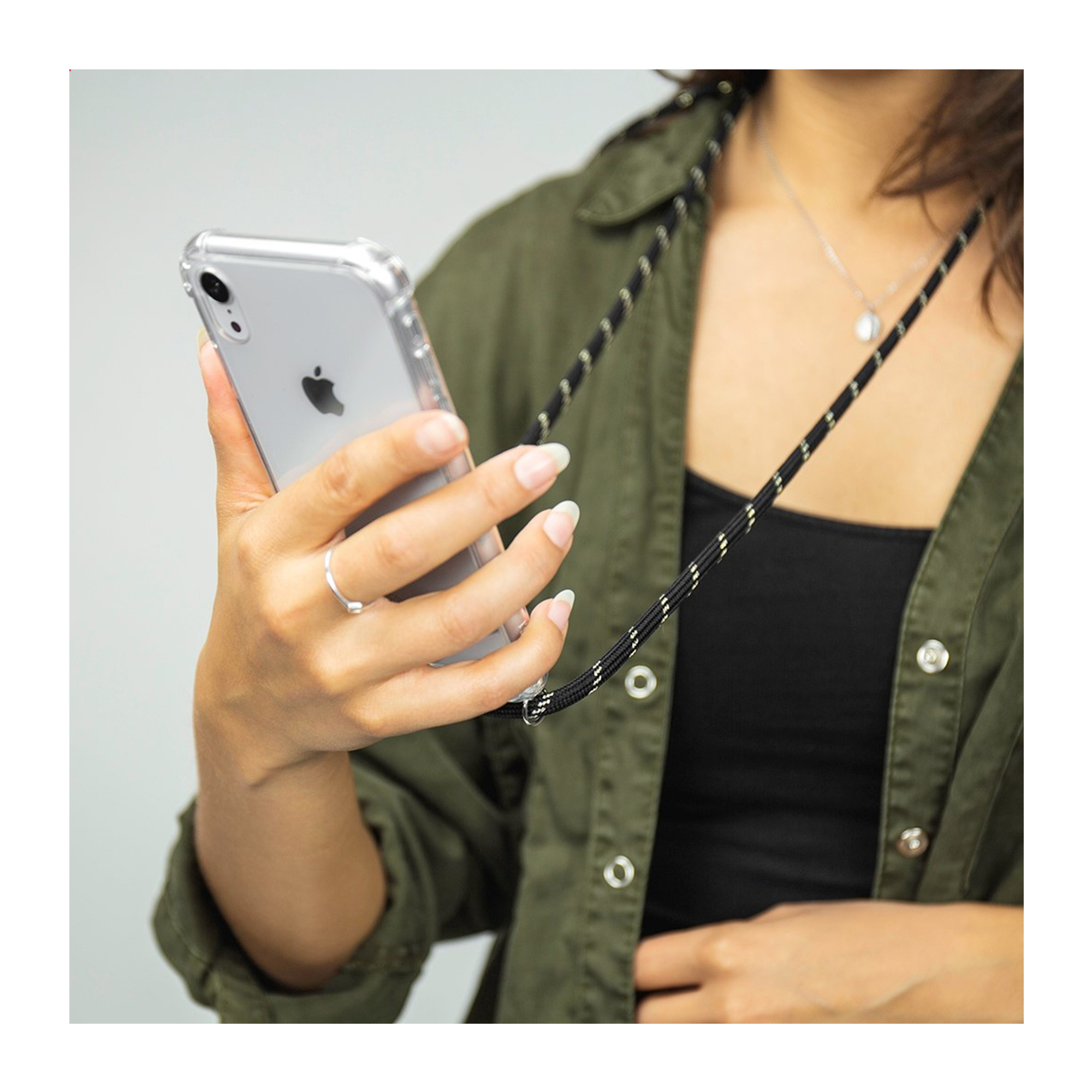 Una persona con chaqueta verde oliva sostiene un iPhone con cordón negro.