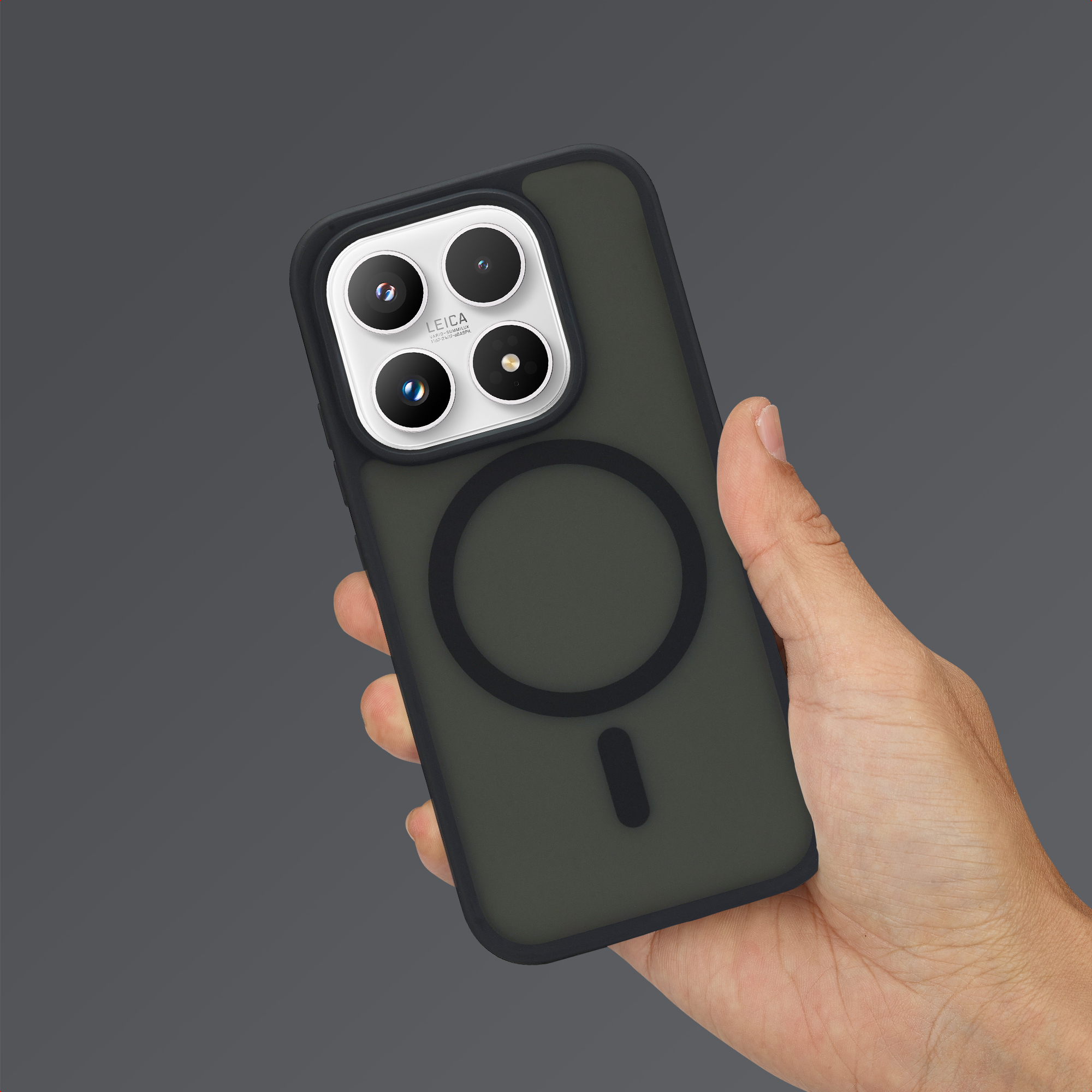 Una mano sostiene un smartphone oscuro en funda con anillo magnético y triple cámara sobre fondo gris.