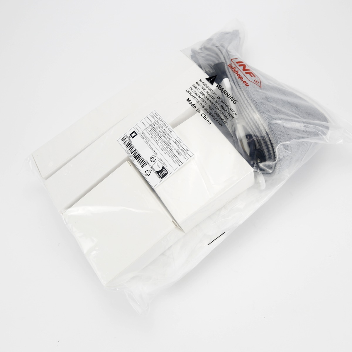 Quattro oggetti rettangolari bianchi e un tessuto grigio in un sacchetto di plastica sigillato con etichette di avvertenza.