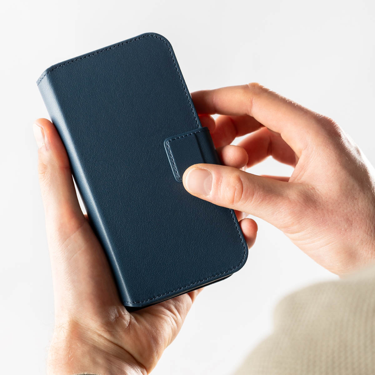 Persona sosteniendo una funda abatible para smartphone de cuero azul oscuro cerrada.