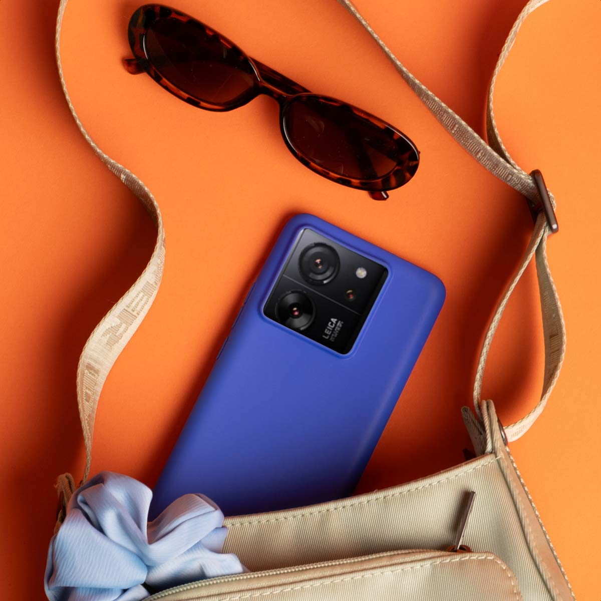 Un smartphone azul, gafas de sol y un bolso sobre fondo naranja.