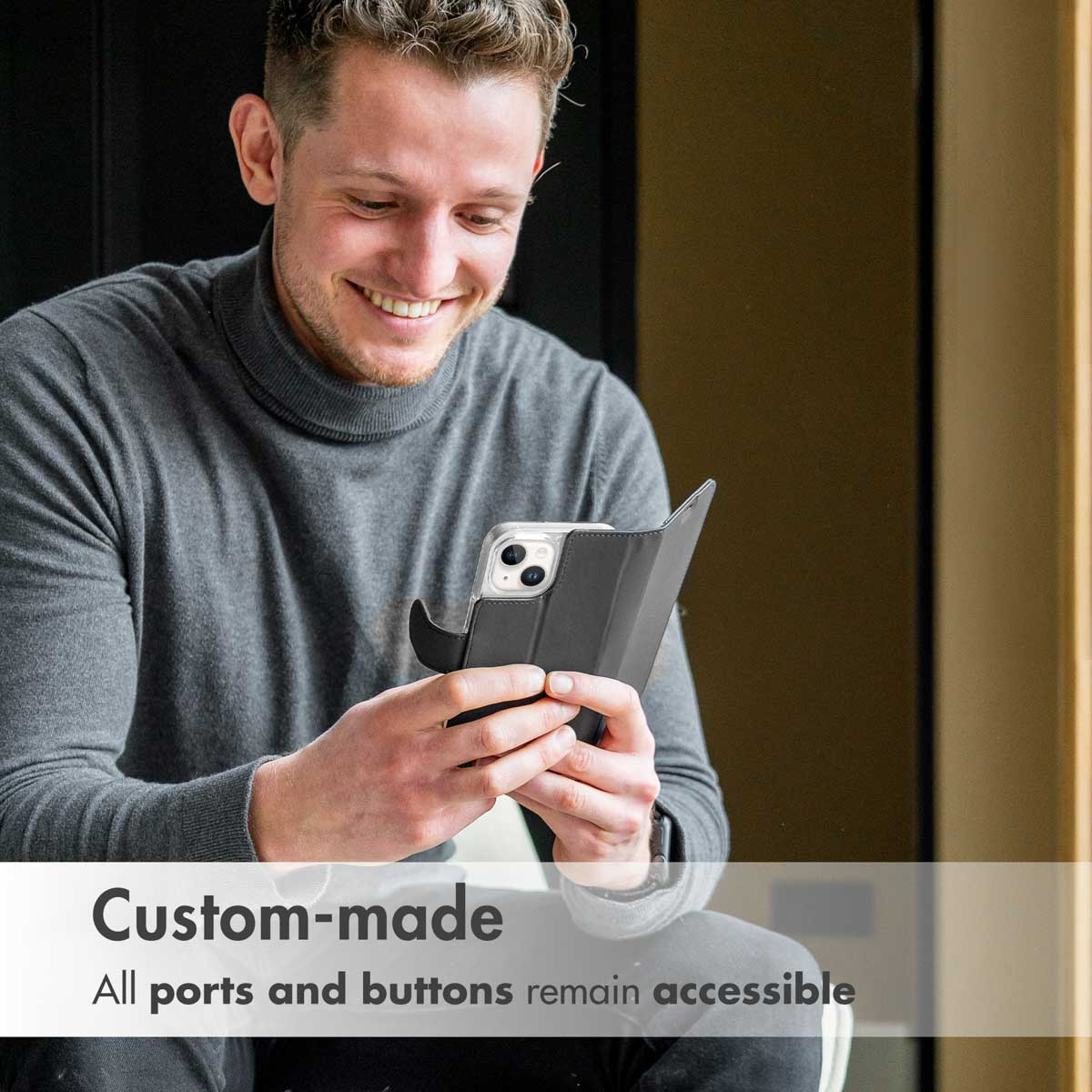 Hombre sonriente con suéter gris sostiene smartphone con funda negra. Texto: Hecho a medida.