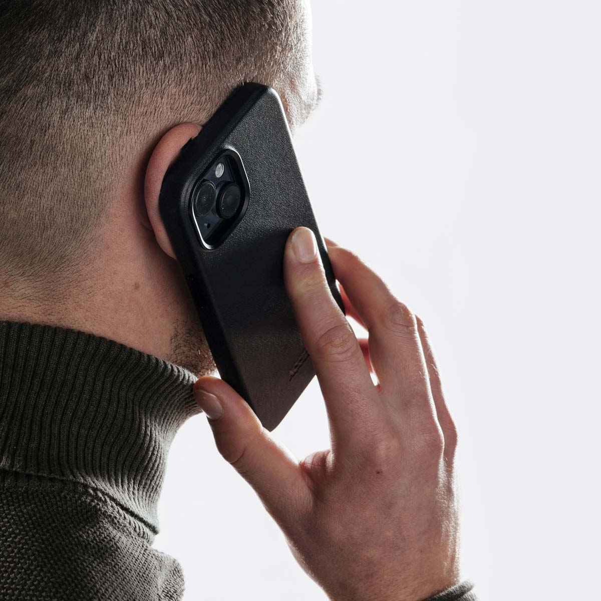 Un uomo che parla con uno smartphone nero su sfondo chiaro.