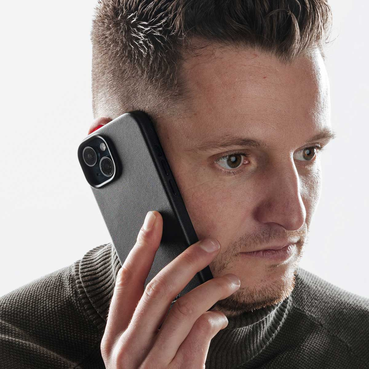 Un uomo con un maglione grigio parla al telefono con uno smartphone nero.