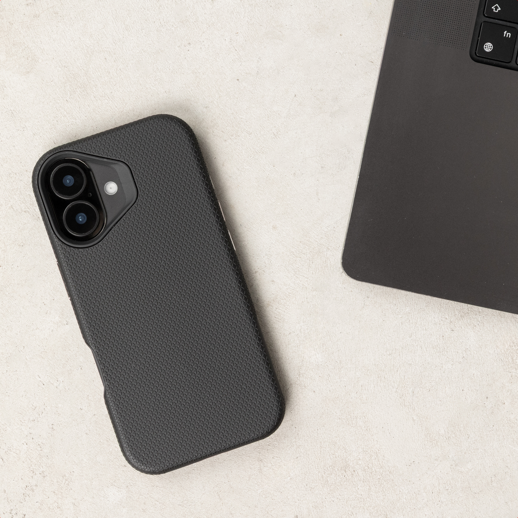 Uno smartphone nero con custodia fantasia si trova accanto alla tastiera di un computer su sfondo chiaro.