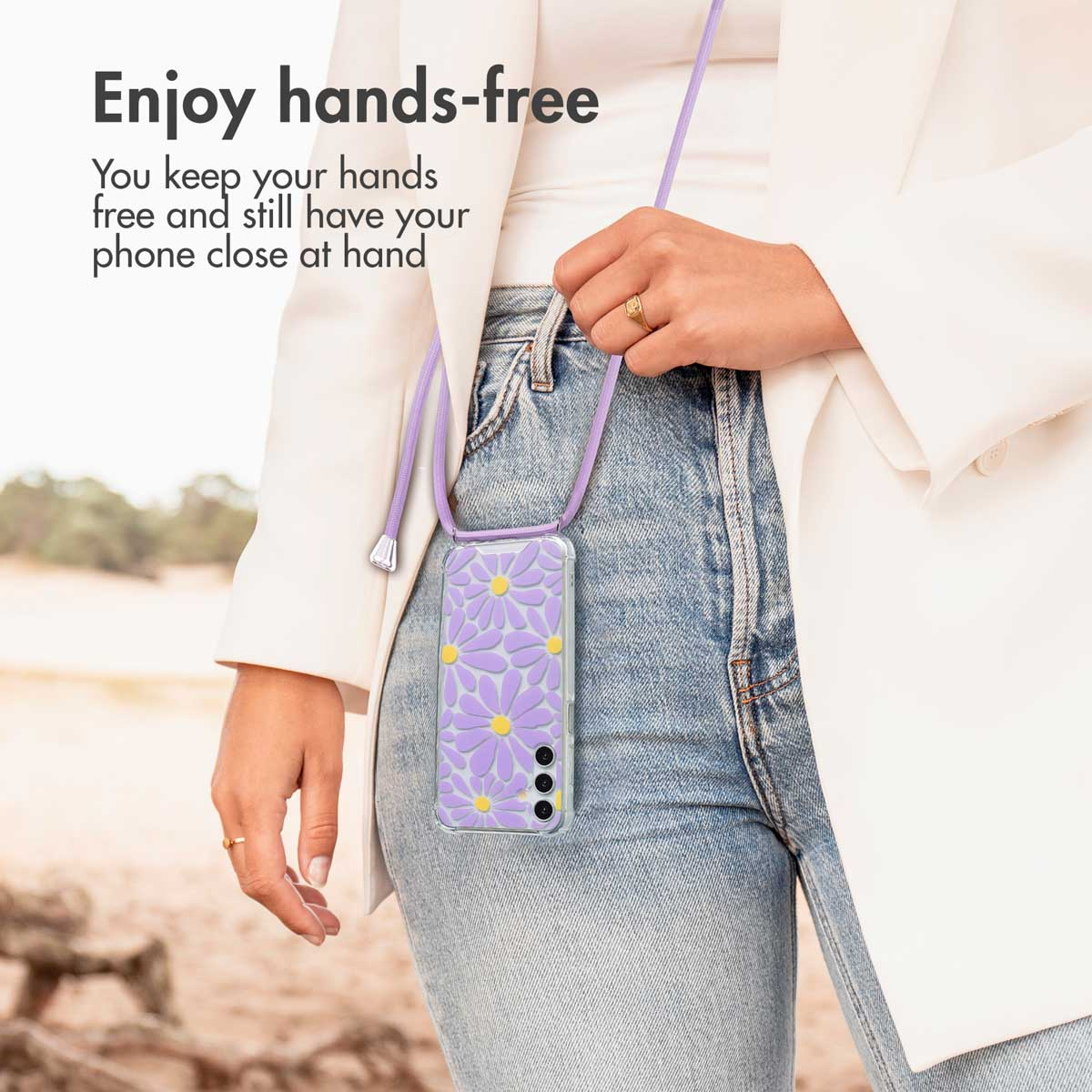 Una donna indossa uno smartphone con custodia floreale viola e tracolla su jeans e giacca bianca.