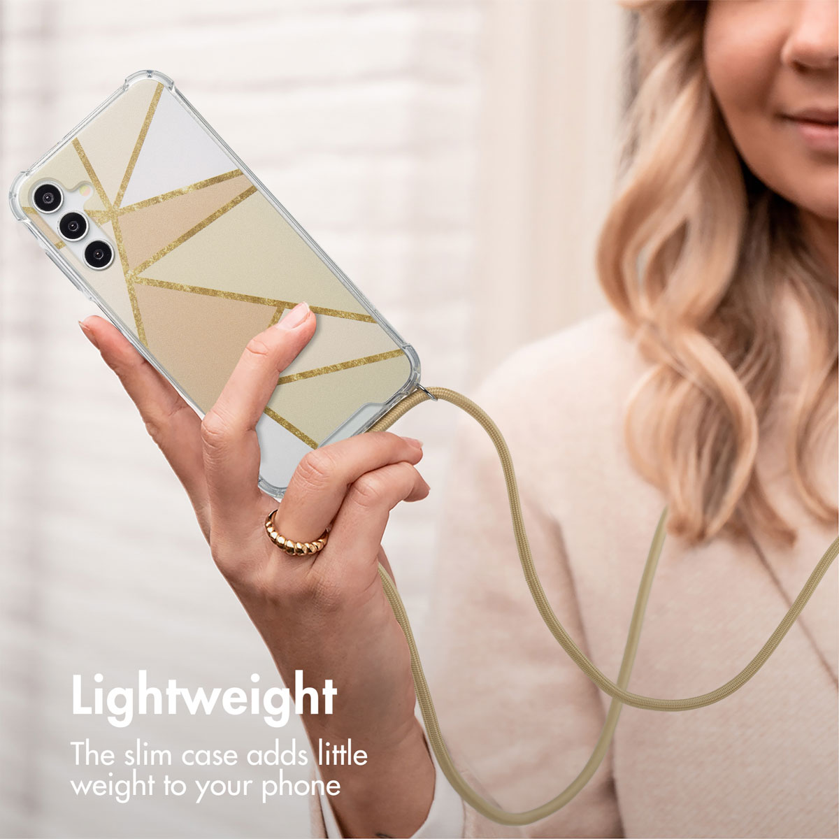 Una donna tiene in mano uno smartphone con cover geometrica dorata e cordino beige.