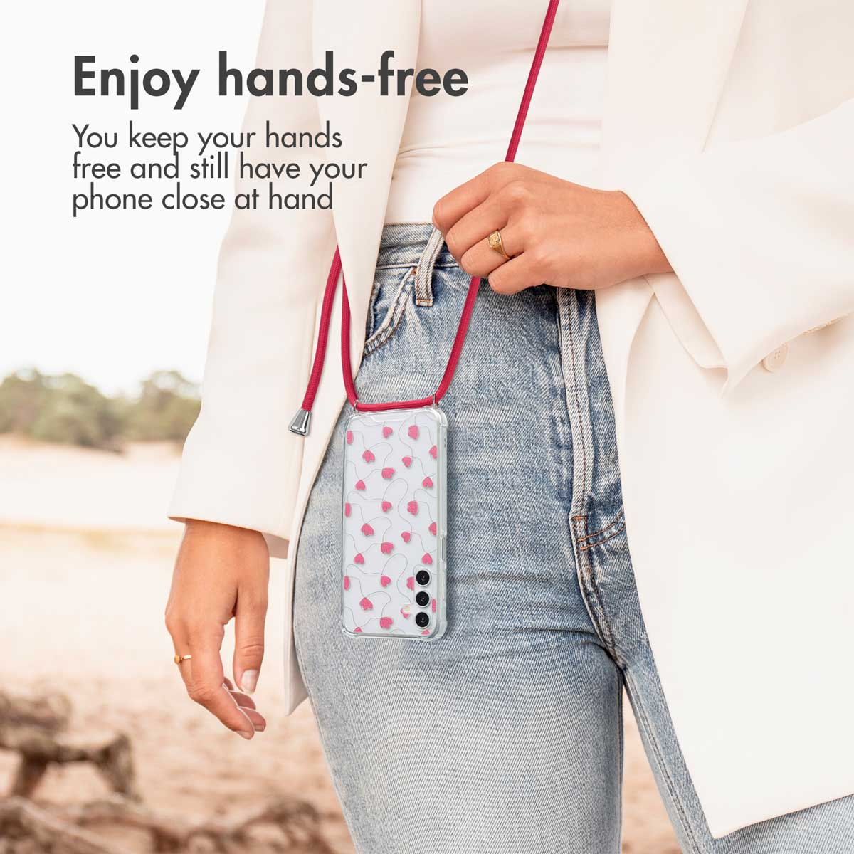 Una donna in giacca bianca e jeans indossa uno smartphone con cordino rosa al collo. Testo: Enjoy hands-free.